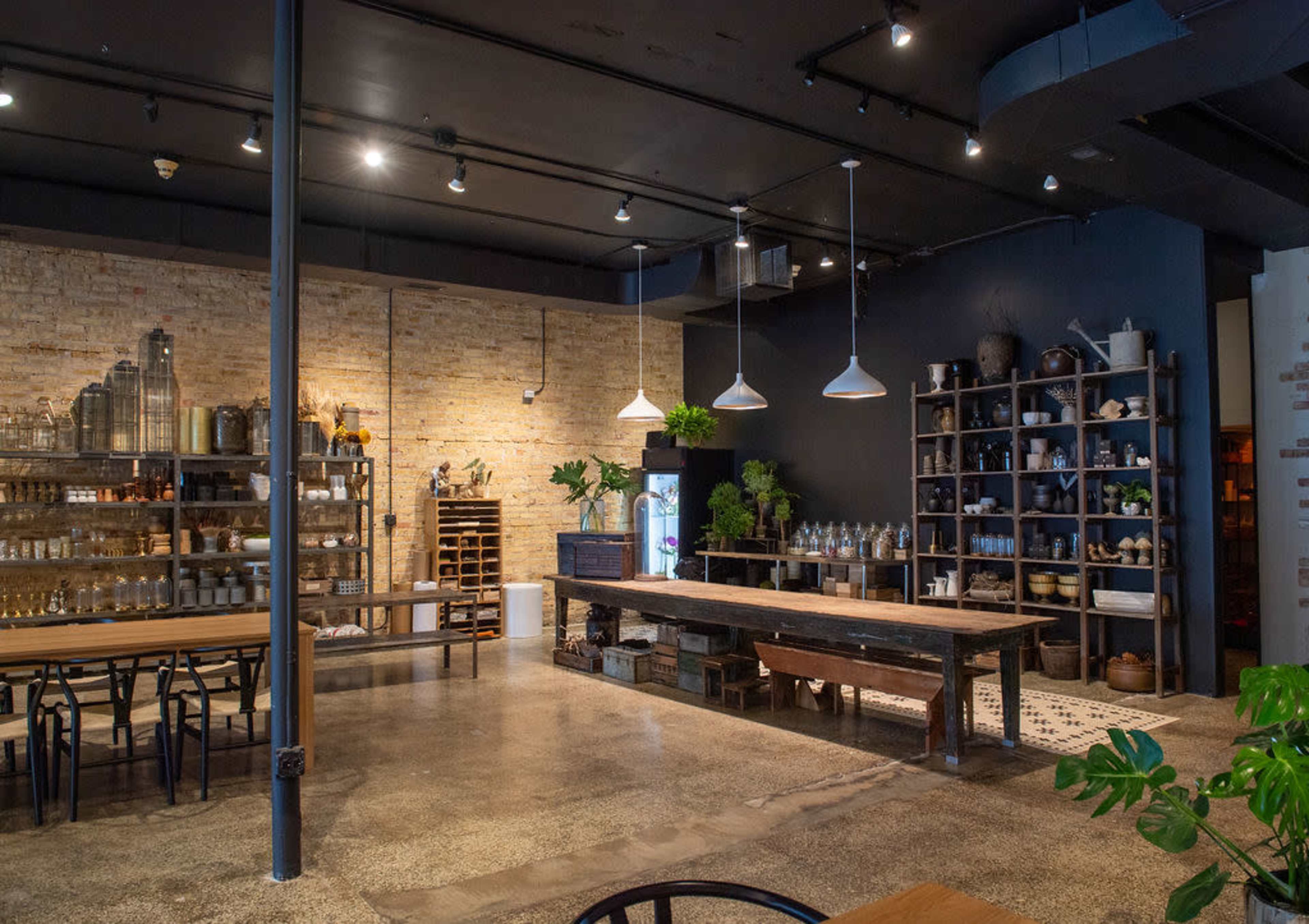 A spacious cafe interior with a mix of wooden furniture, shelves filled with various decorative items, and large windows allowing natural light to enter.