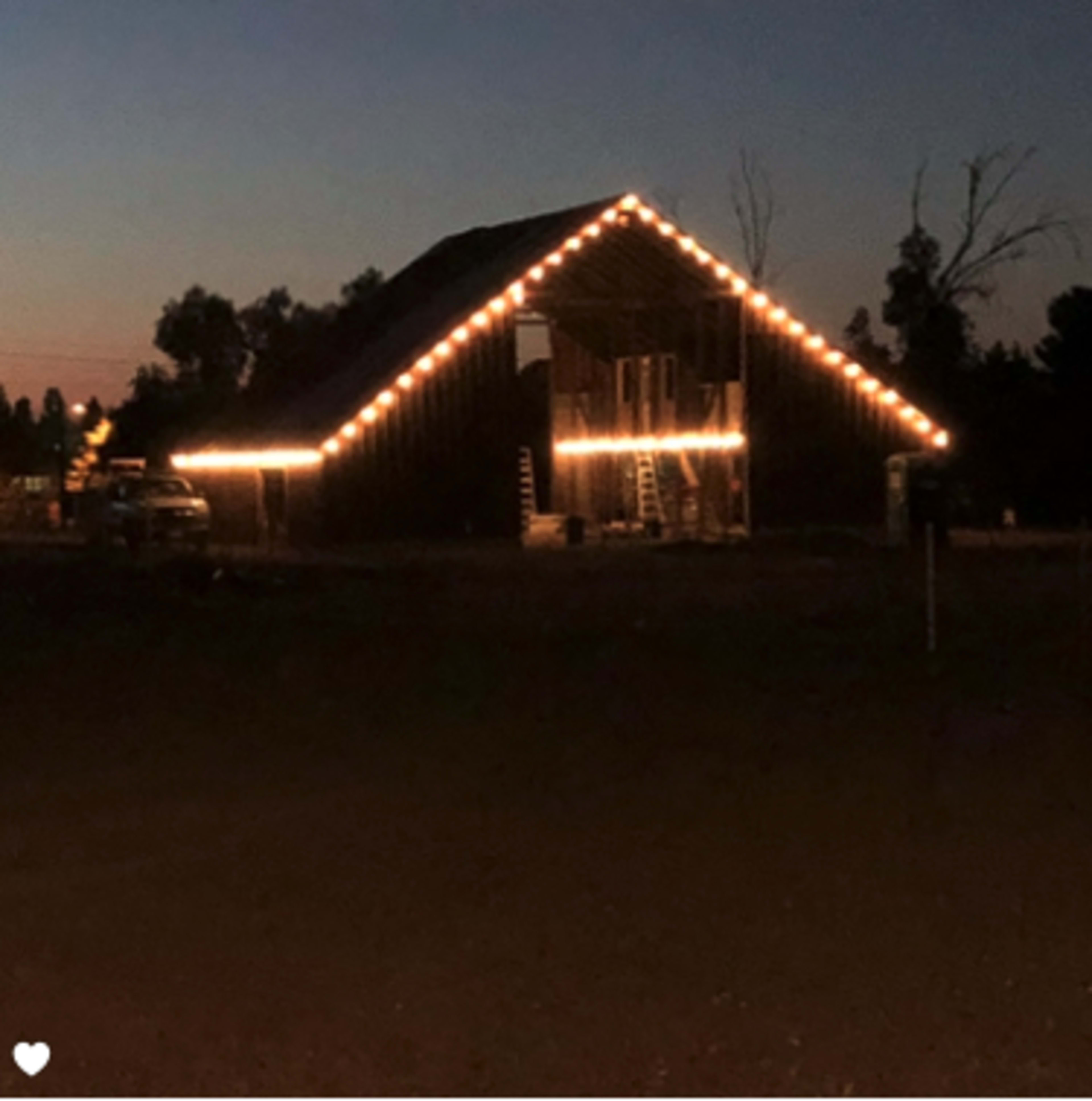 A barn is outlined with string lights against a twilight sky.