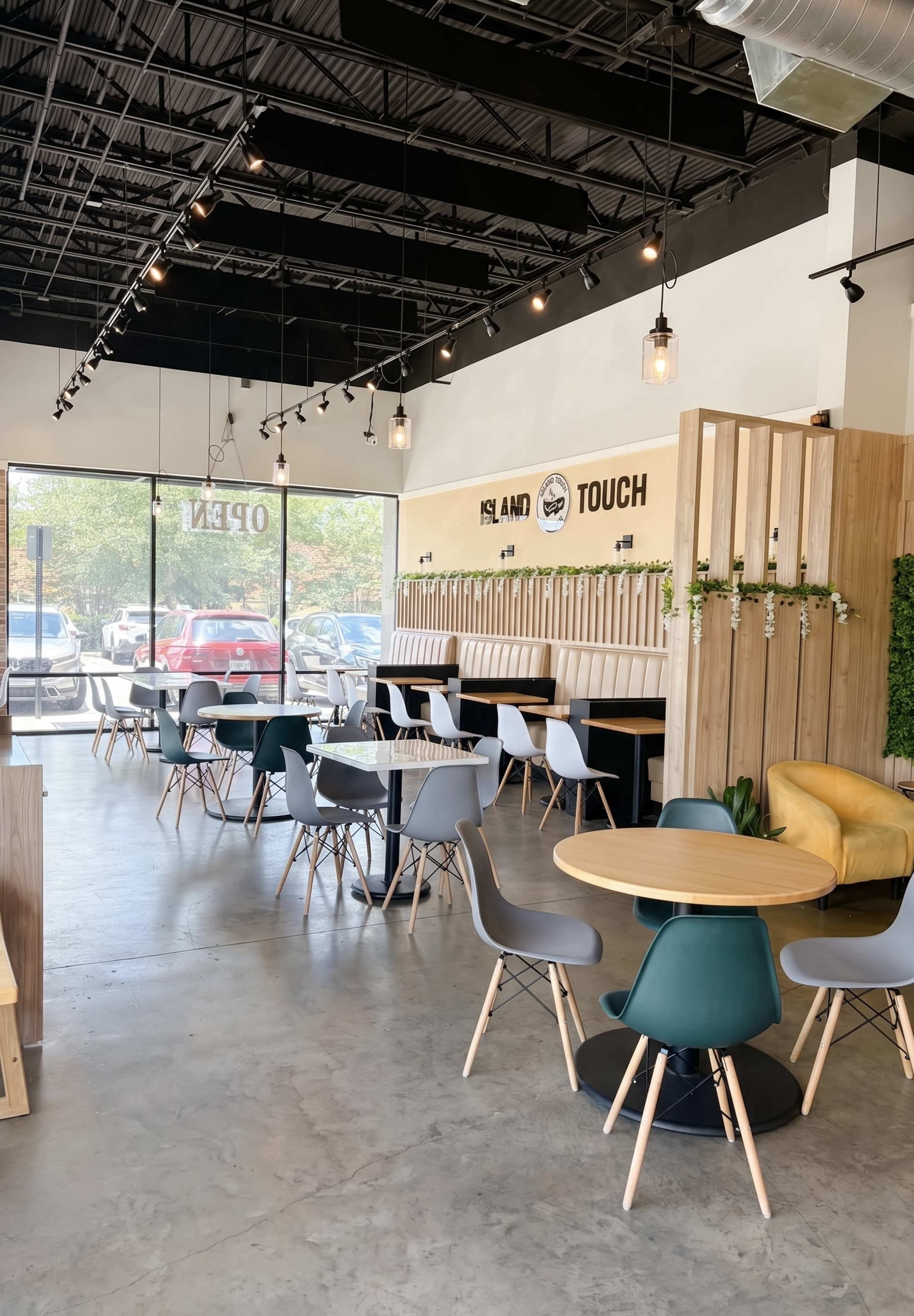 The image shows a modern café interior with wooden accents, various seating arrangements, and large windows allowing natural light.