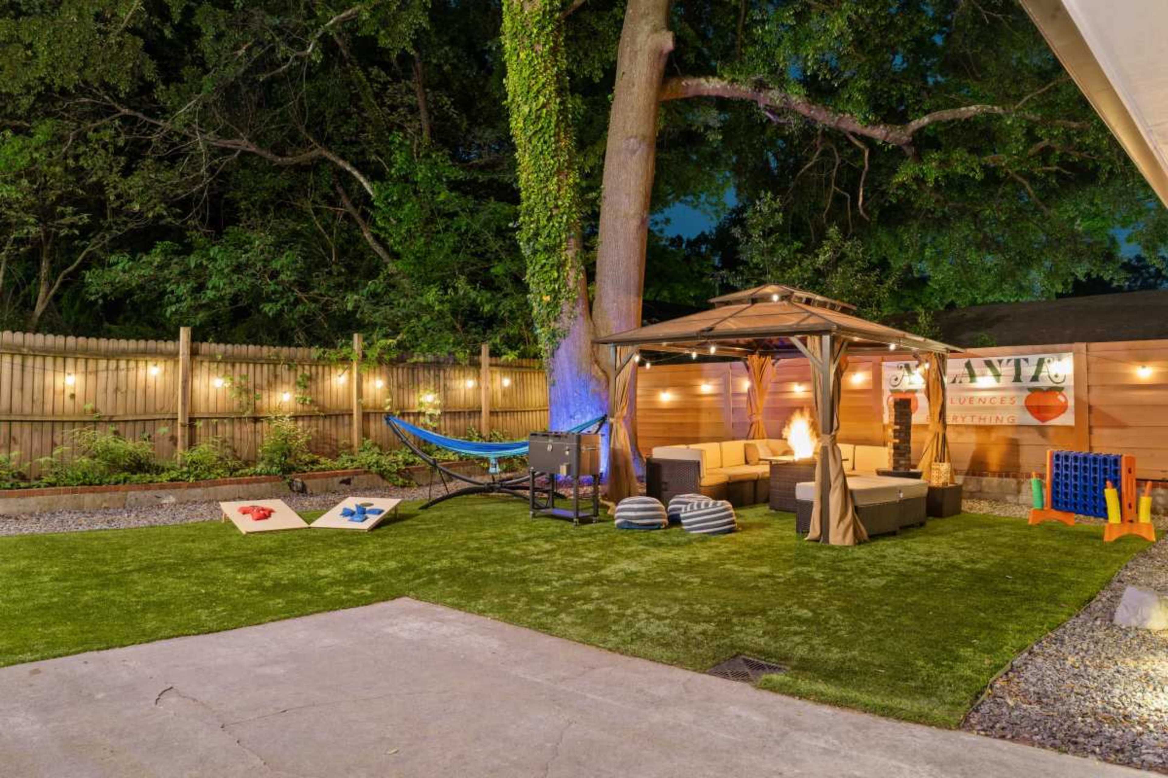 The image shows a yard with a seating area, a hammock, illuminated trees, and a gazebo, all set on artificial grass.