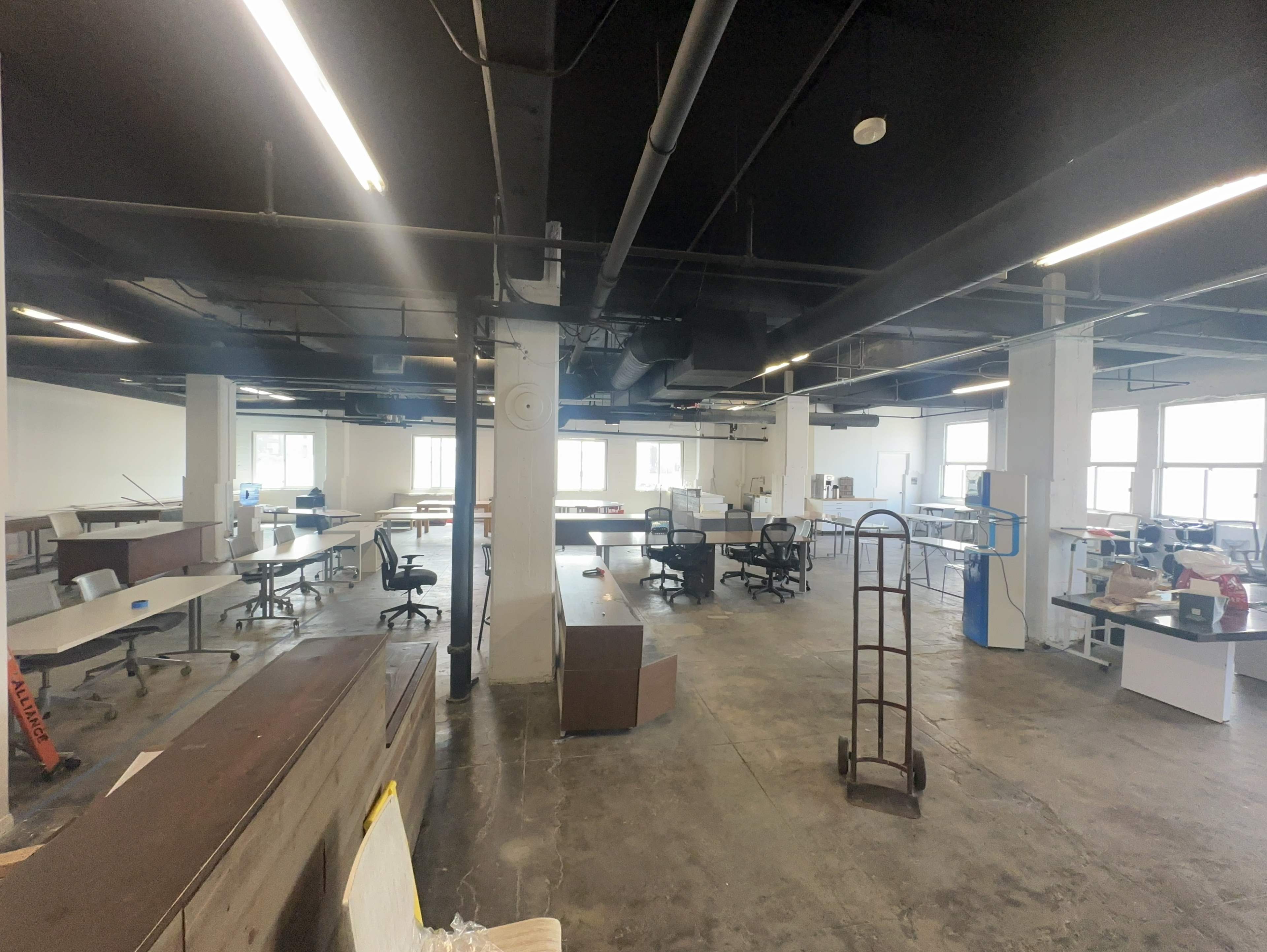 An empty office space with desks, chairs, and various equipment arranged throughout.