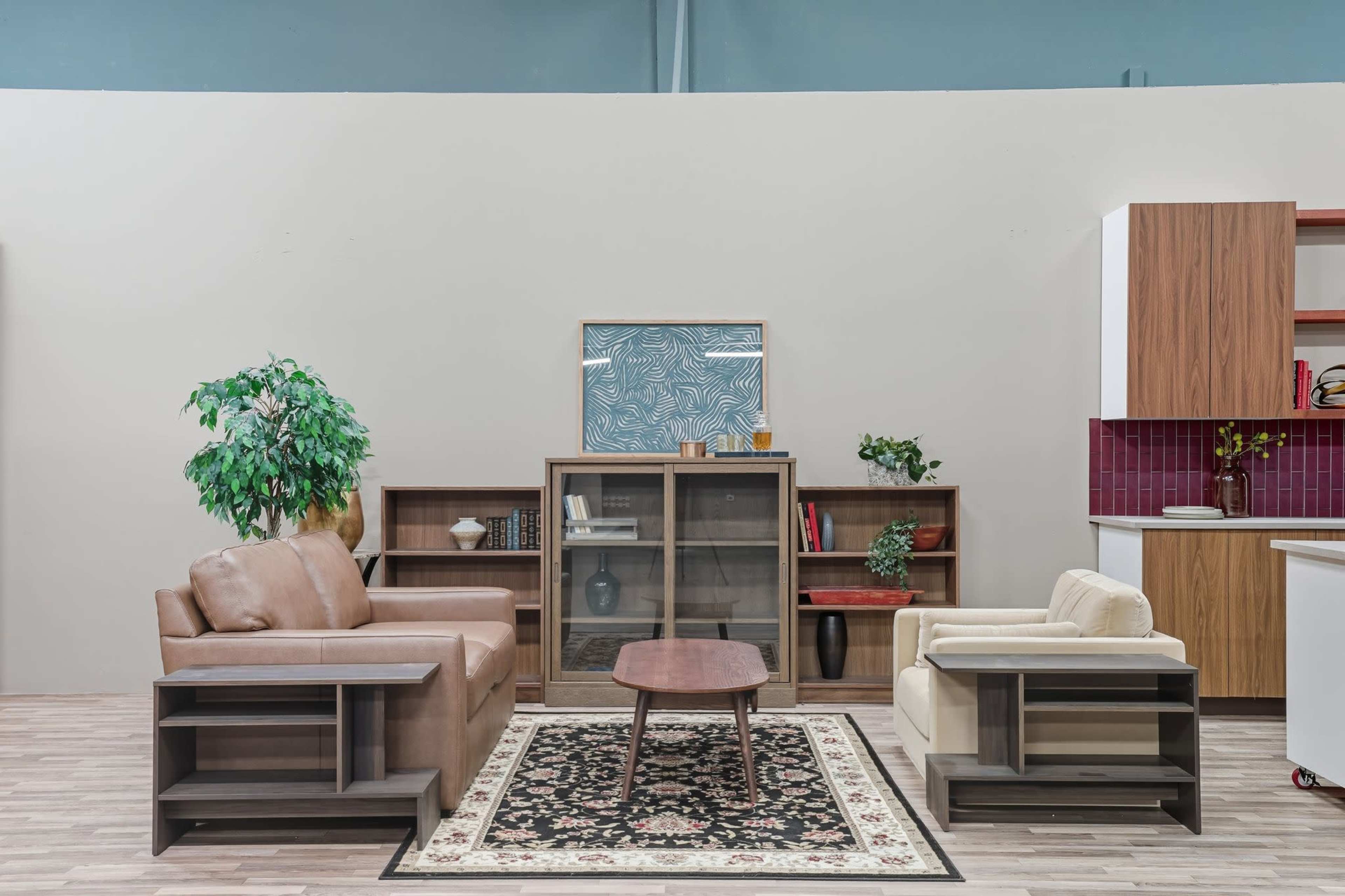 A living room setup features a brown leather sofa and a beige armchair, accompanied by a wooden coffee table and bookshelves against a light-colored wall.