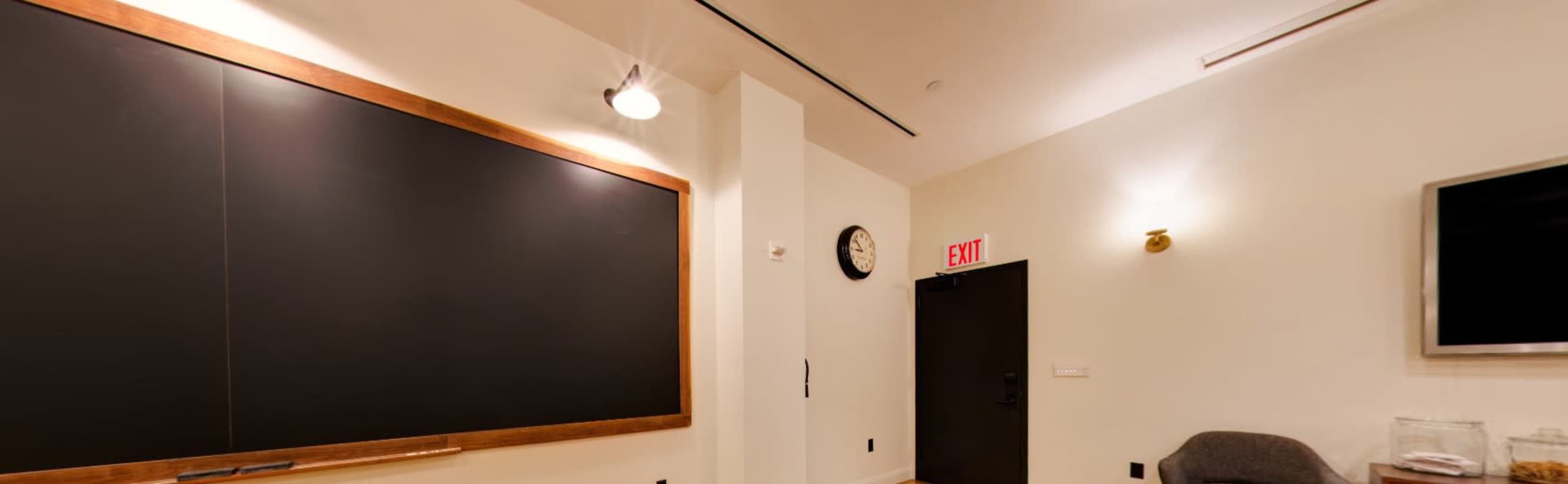 The image shows a classroom with a black chalkboard, a wall clock, and an exit door.