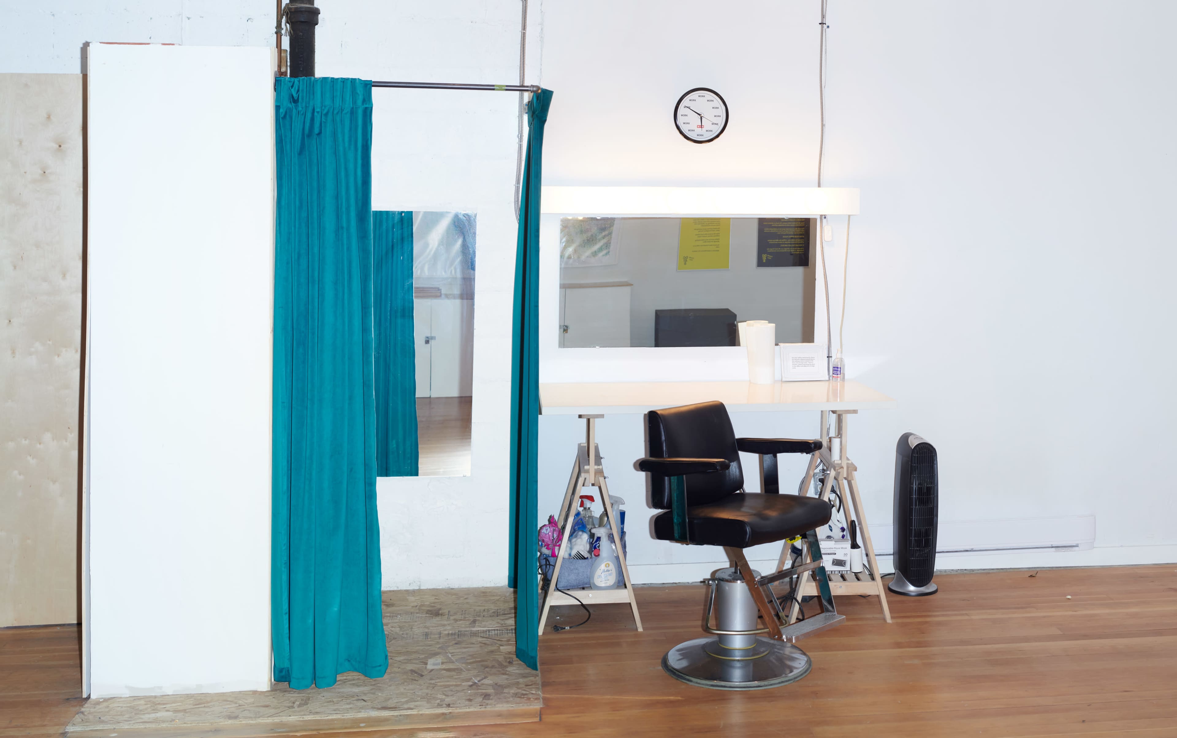 A hair salon setup featuring a black barber's chair, a mirror with a lighted frame, and a curtain separating a section of the space.