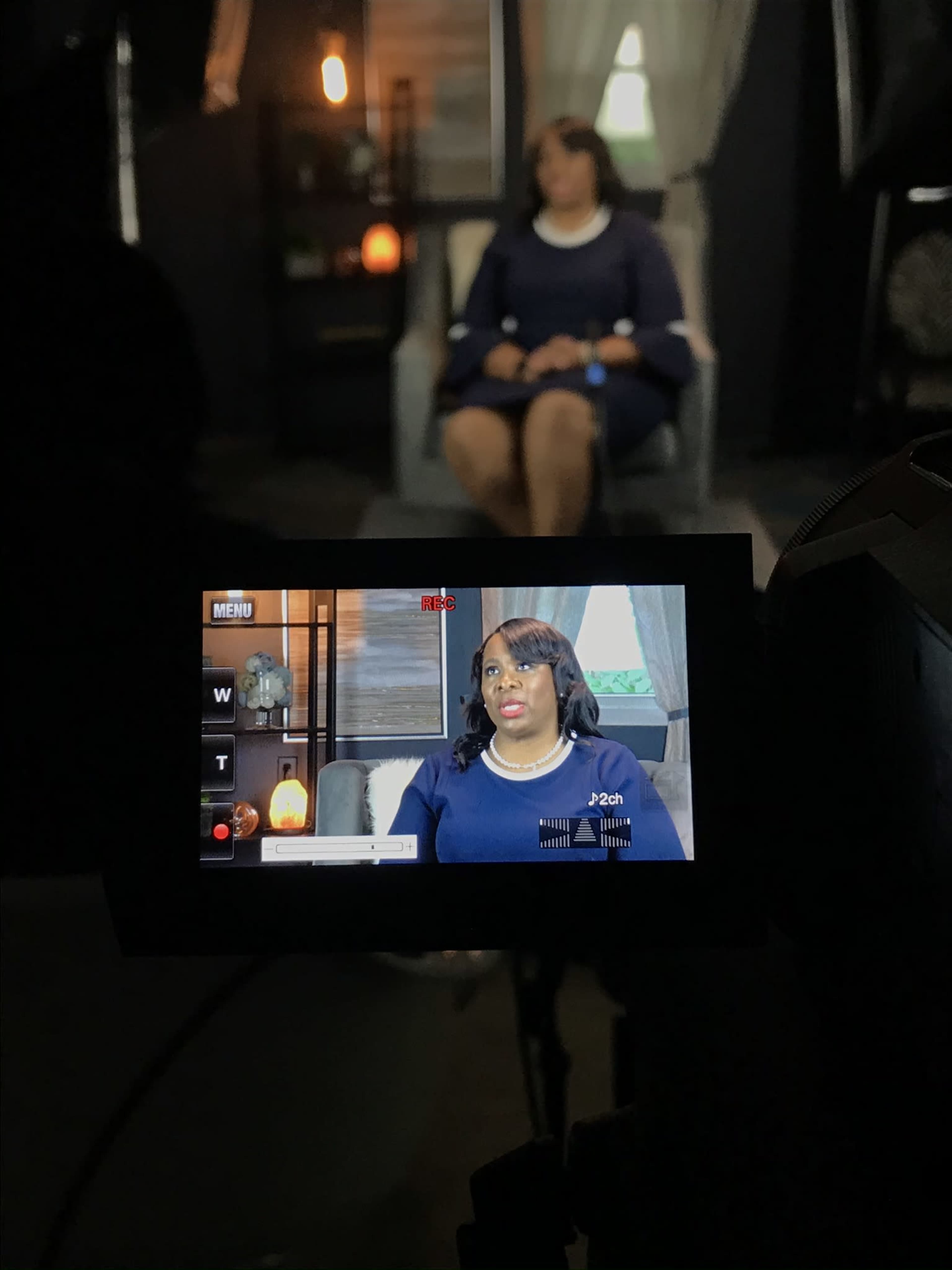 A woman is being filmed while sitting in a chair in a dimly lit room.