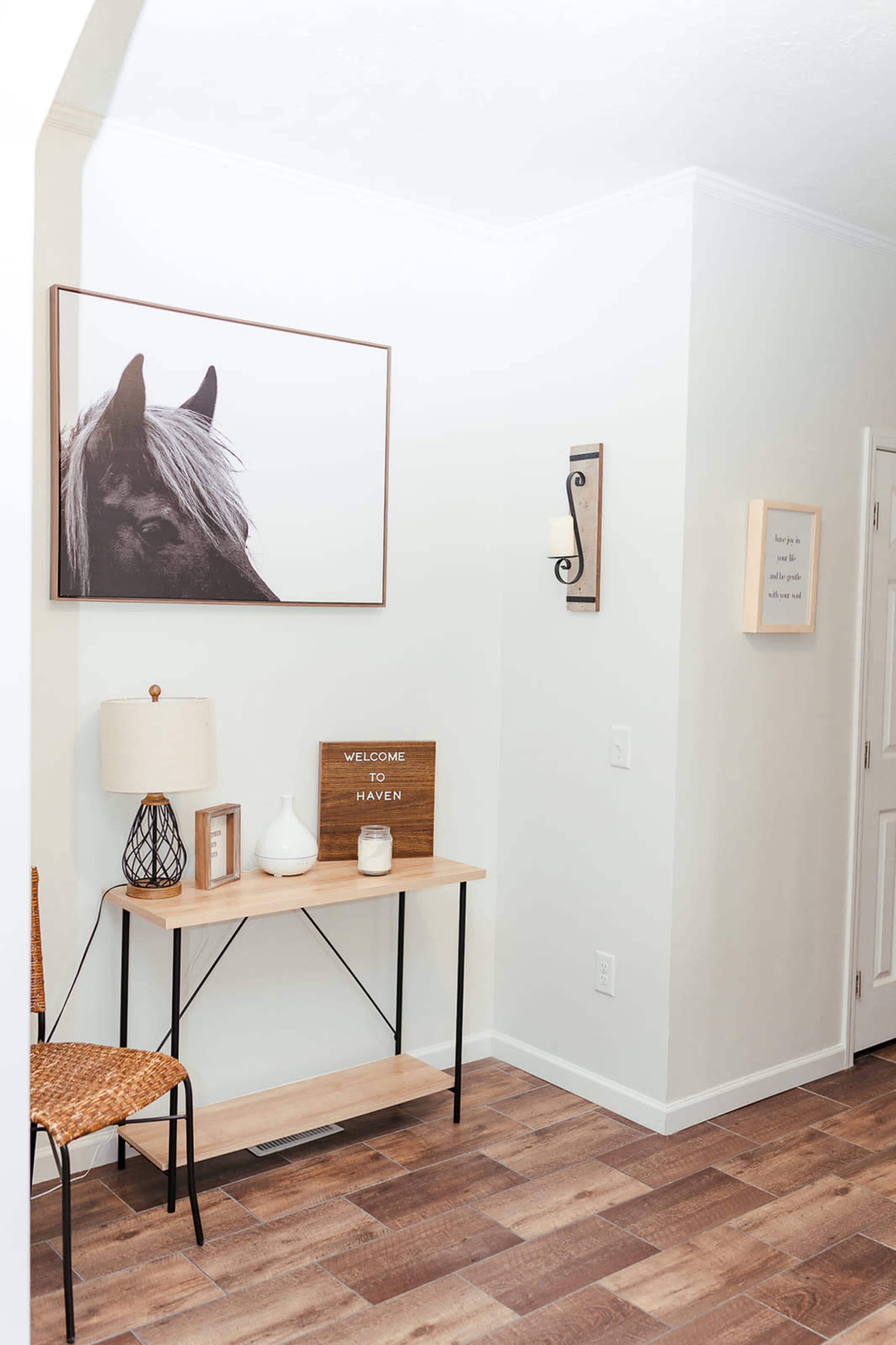 A horse portrait hangs above a wooden table that displays decorative items and a welcome sign in a well-lit entryway.