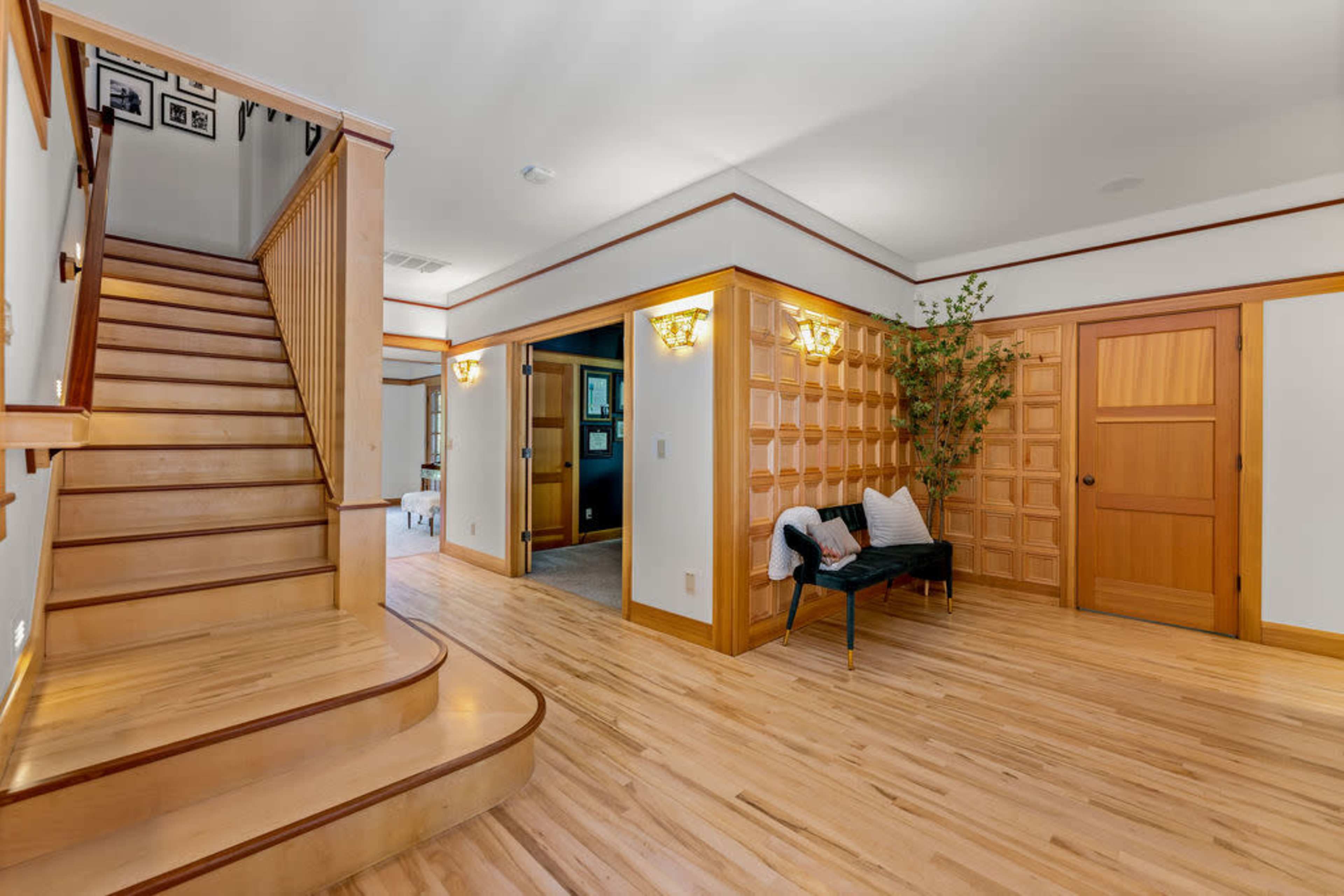 A wooden staircase leading to an upper level, with a hallway featuring decorative wall paneling and a small seating area.