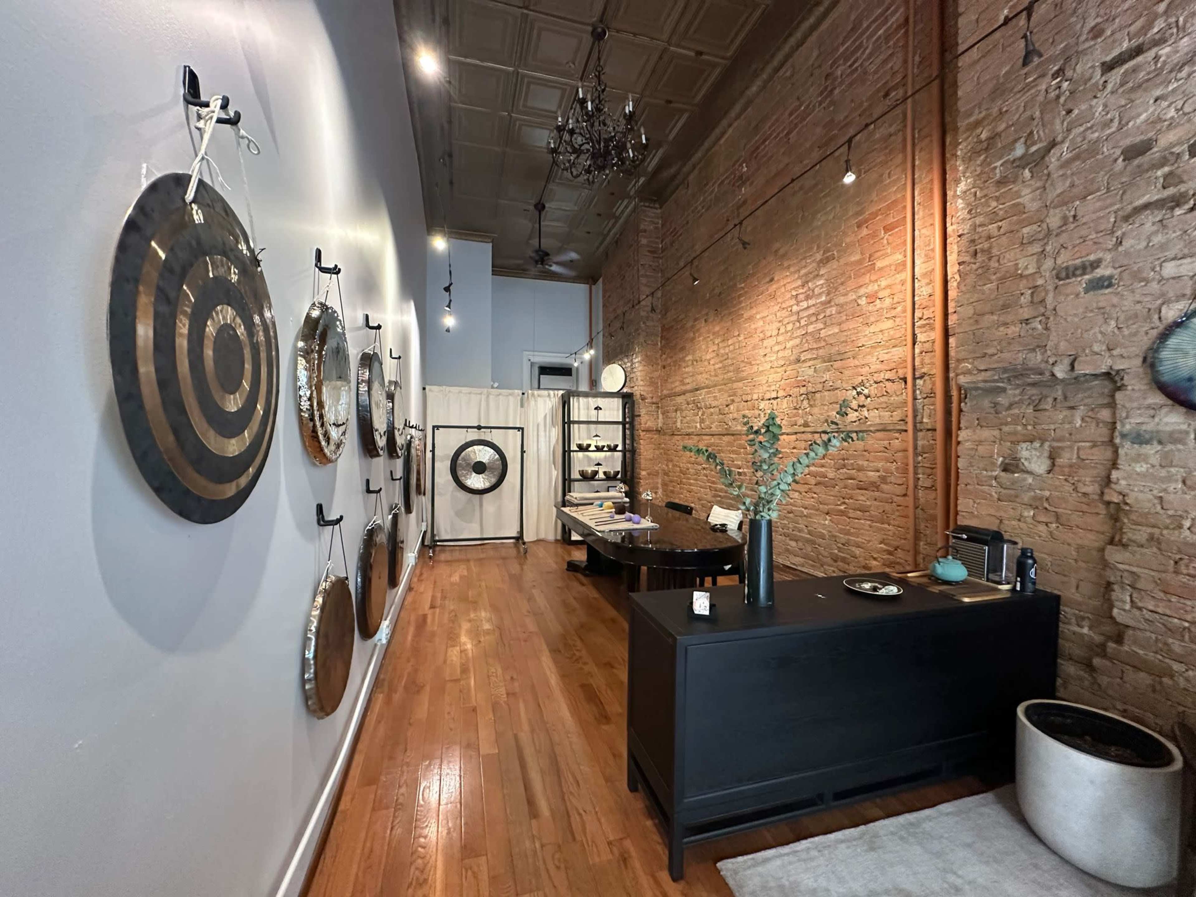The image shows an interior of a shop with exposed brick walls, featuring decorative circular wall art, a black reception desk, and wooden flooring.