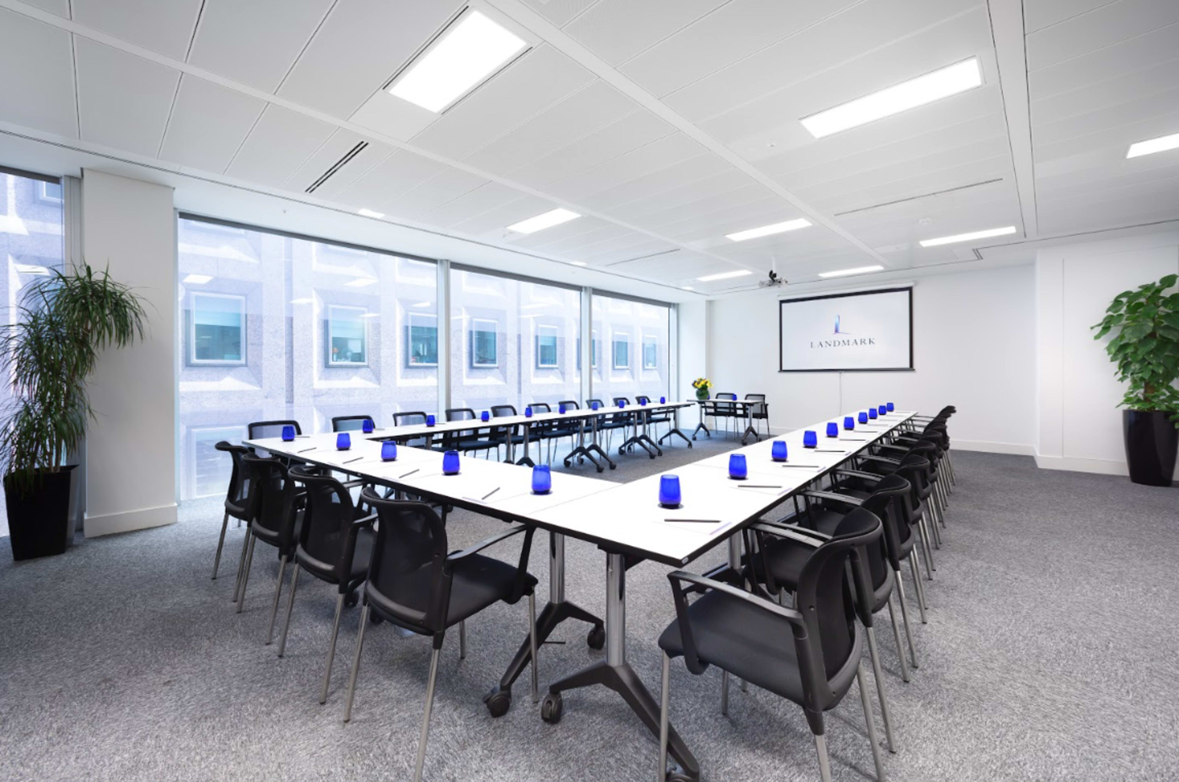 A spacious conference room features a large rectangular table surrounded by black chairs, illuminated by natural light streaming through large windows.