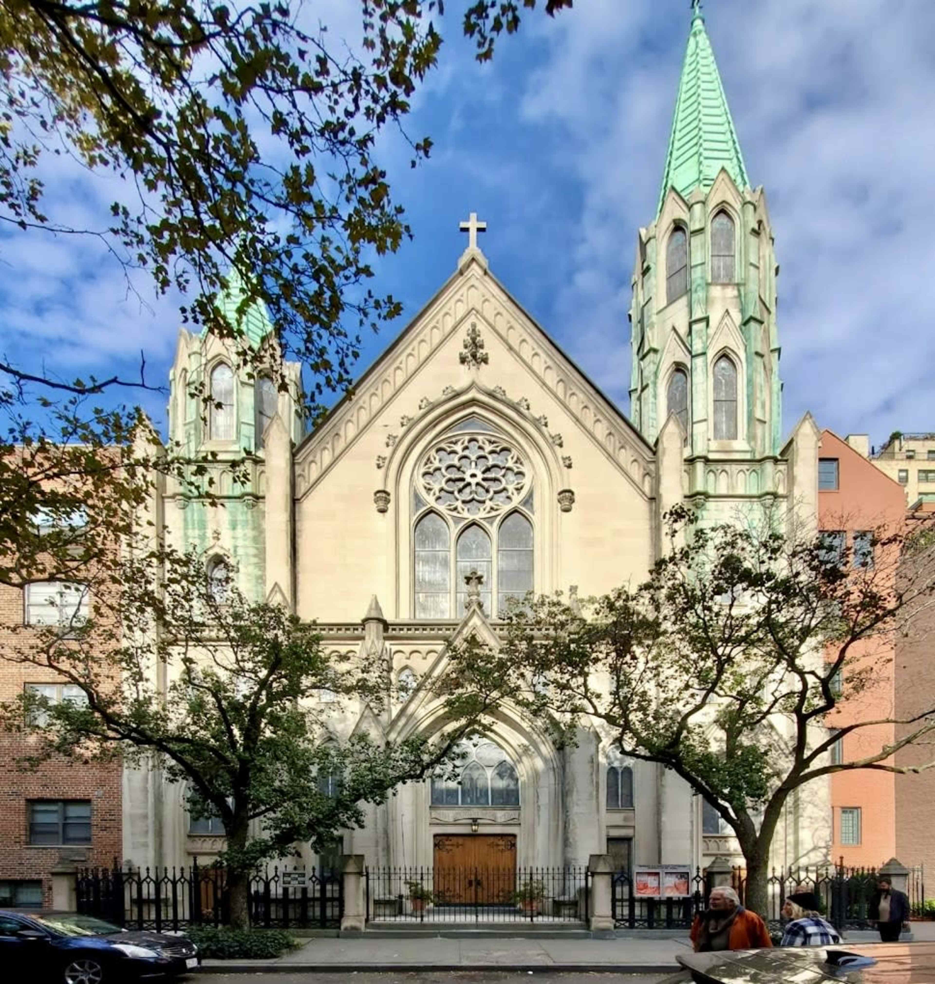 A large church with a Gothic architectural style featuring two tall spires and a large rose window, surrounded by trees and buildings.