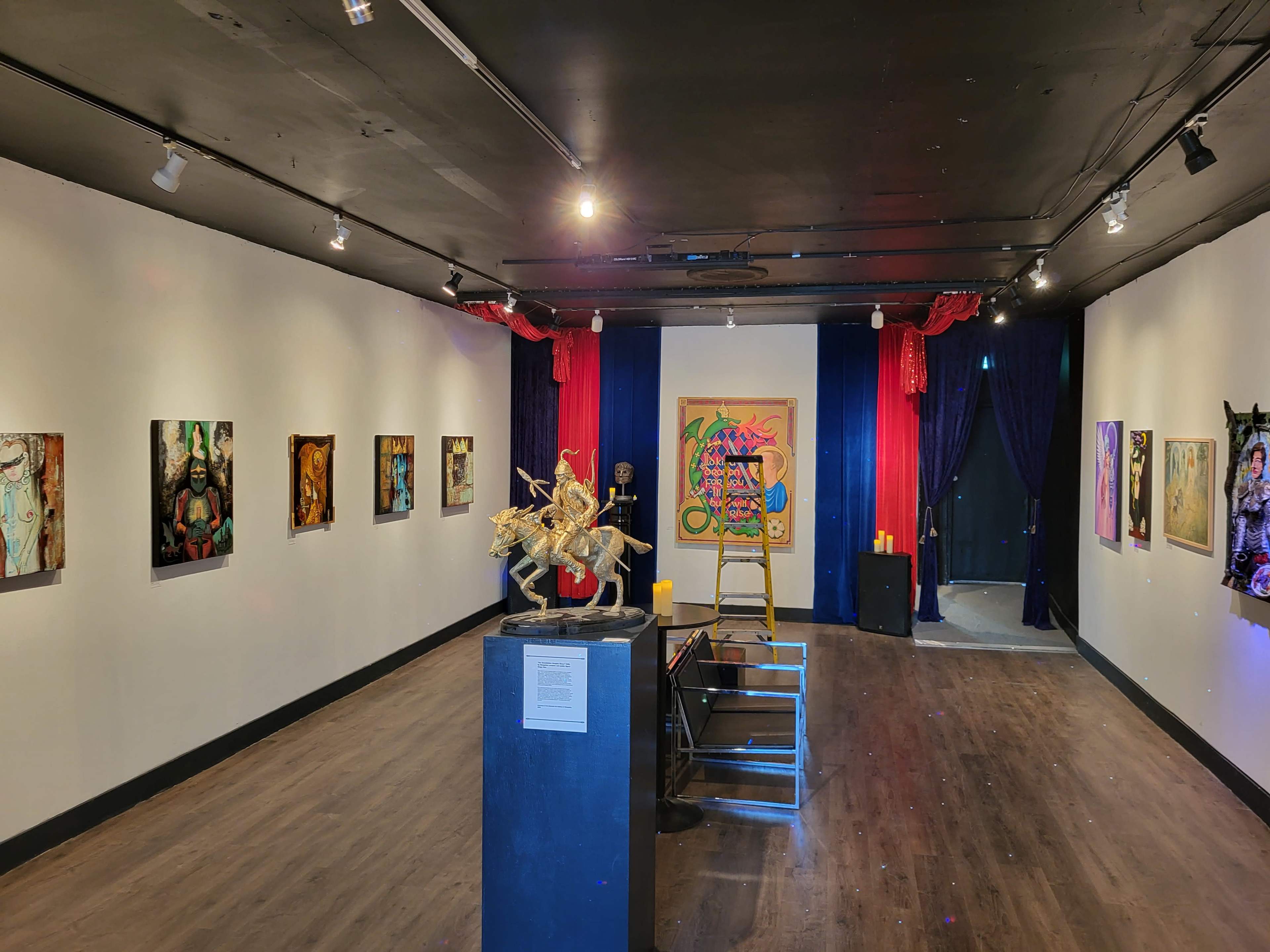 An art gallery featuring various paintings on the walls, a sculpture on a pedestal, and a ladder positioned near the center of the room.