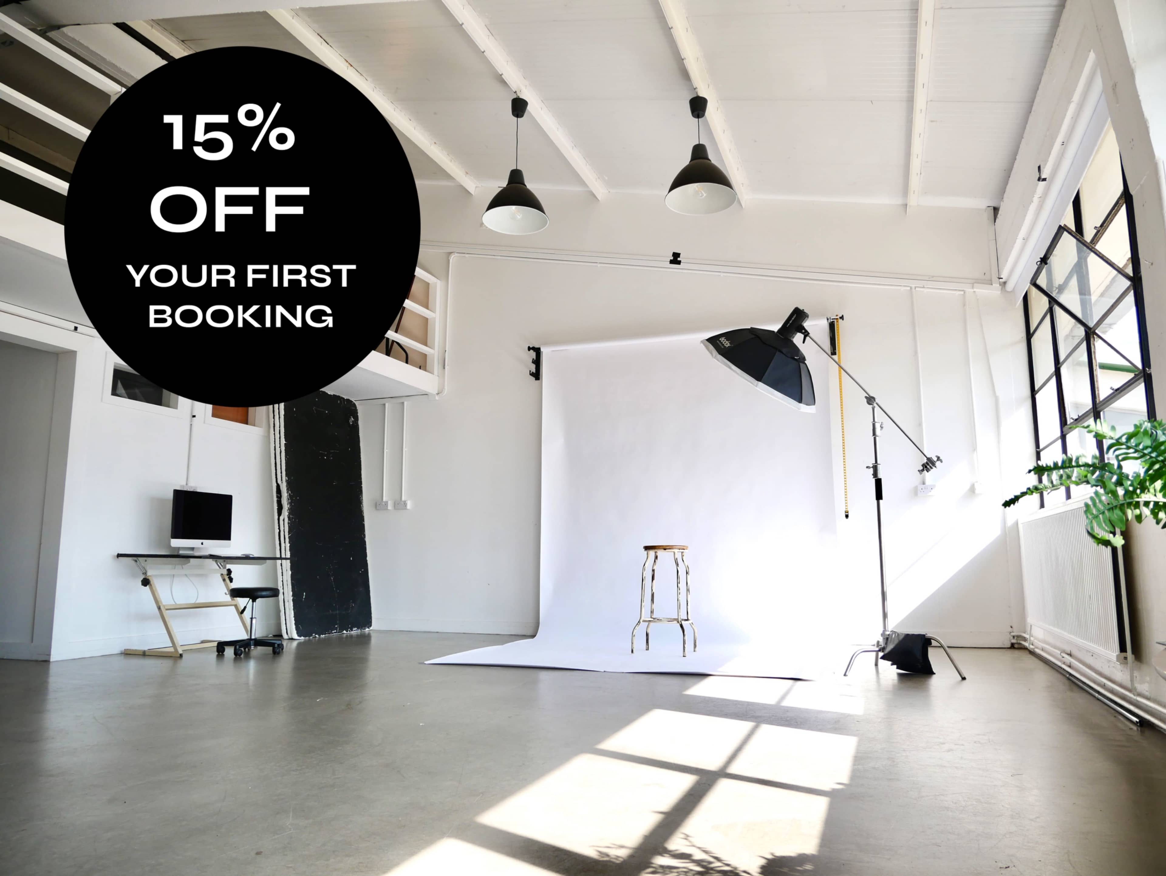The image shows a spacious photography studio with a white backdrop, a stool, and equipment set up for a shoot.