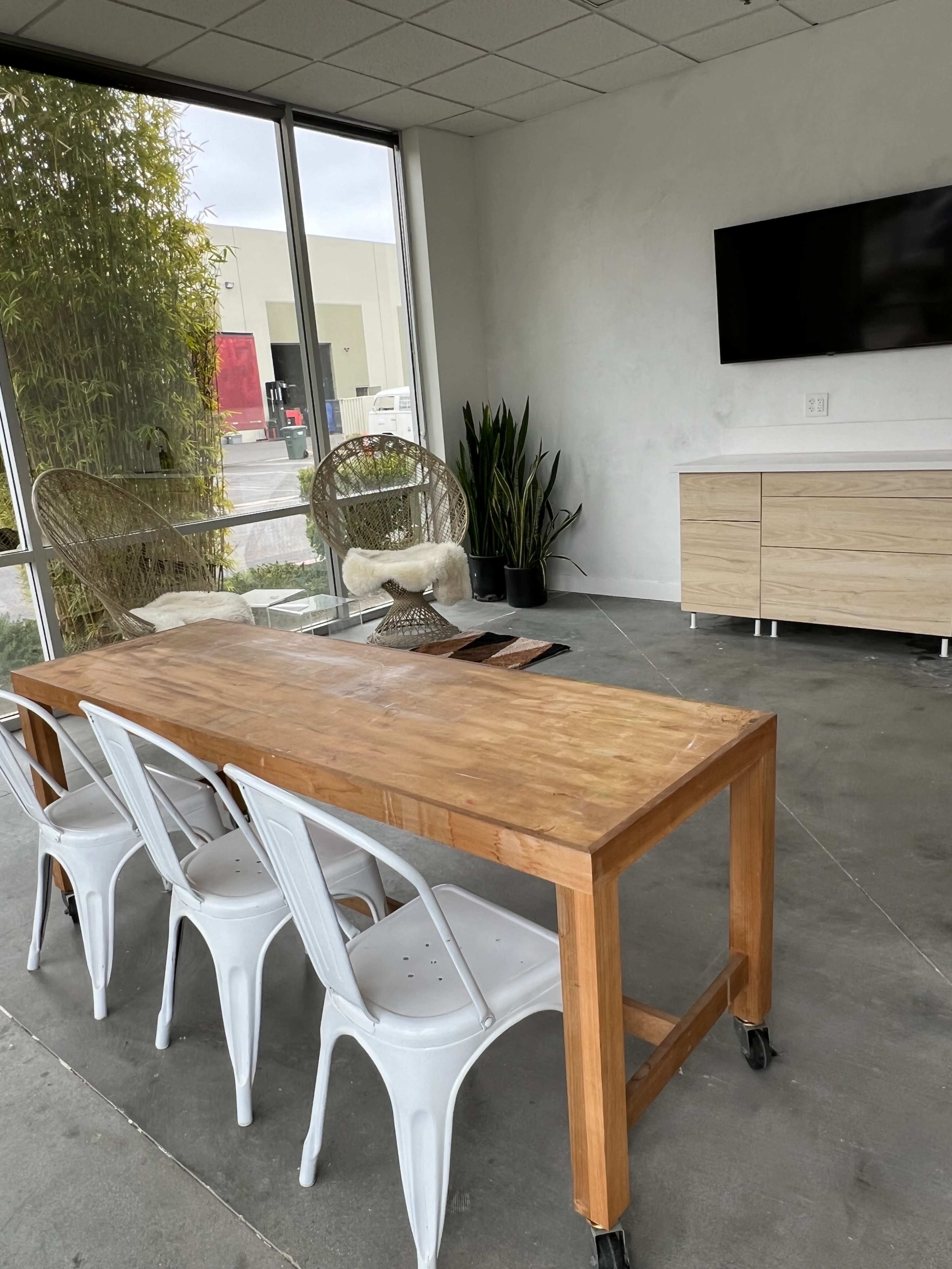 A wooden table with four metal chairs is positioned in a modern, light-filled room featuring large windows and minimalistic furniture.