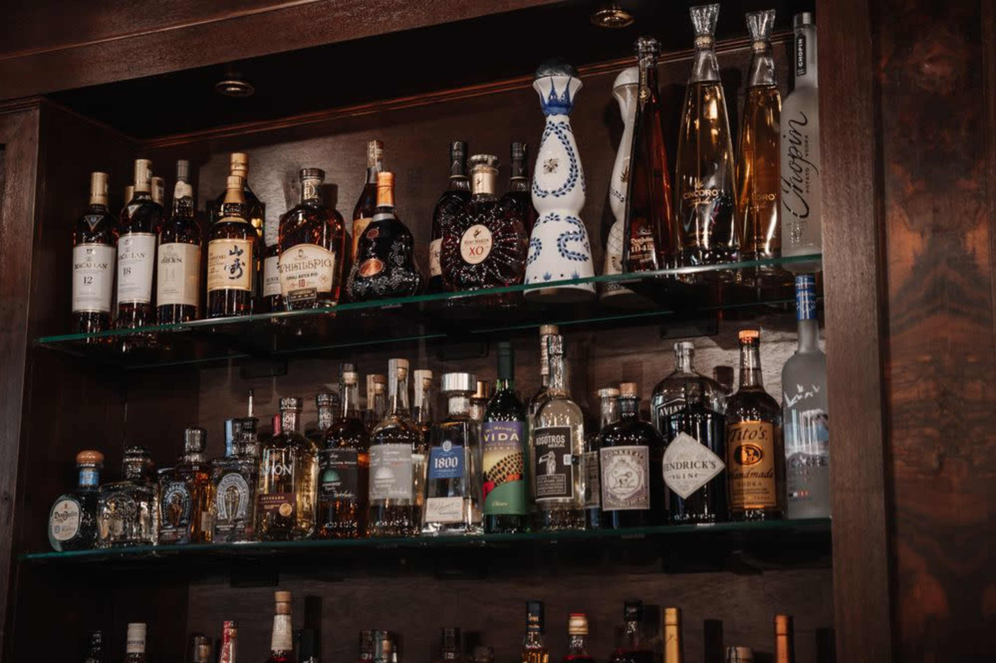 A wooden shelf displays a variety of alcoholic beverages, including bottles of whiskey, tequila, vodka, and other spirits, arranged in an orderly fashion.