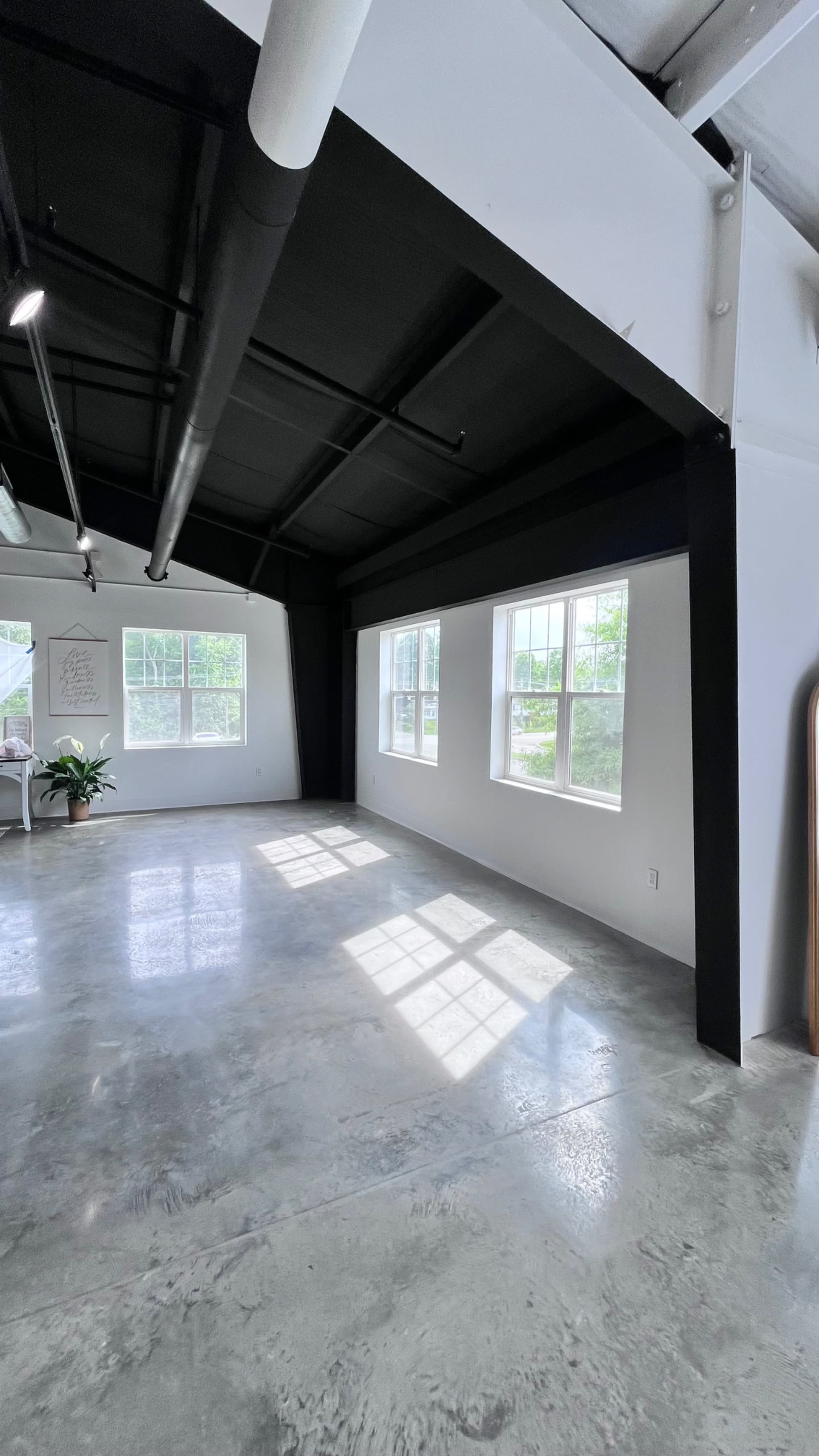 The image shows a spacious interior with polished concrete floors, large windows, and a black ceiling in a well-lit room.