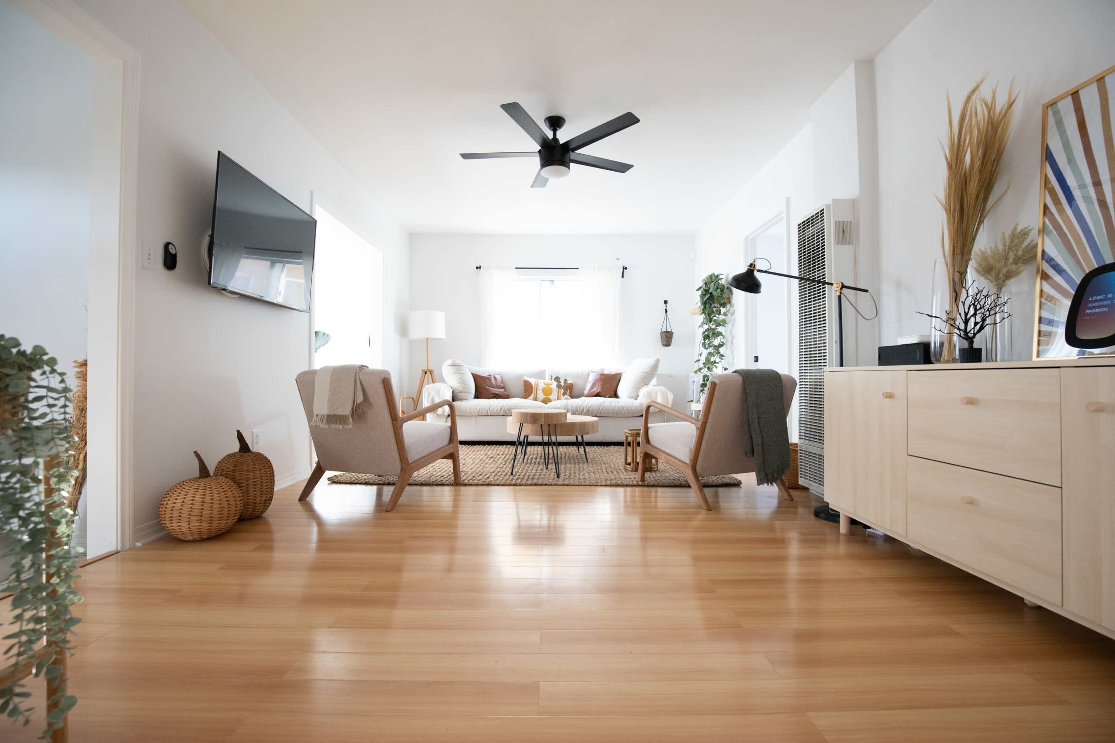 A bright living room features a seating area with a sofa, two armchairs, and a wooden coffee table on a light-colored rug.