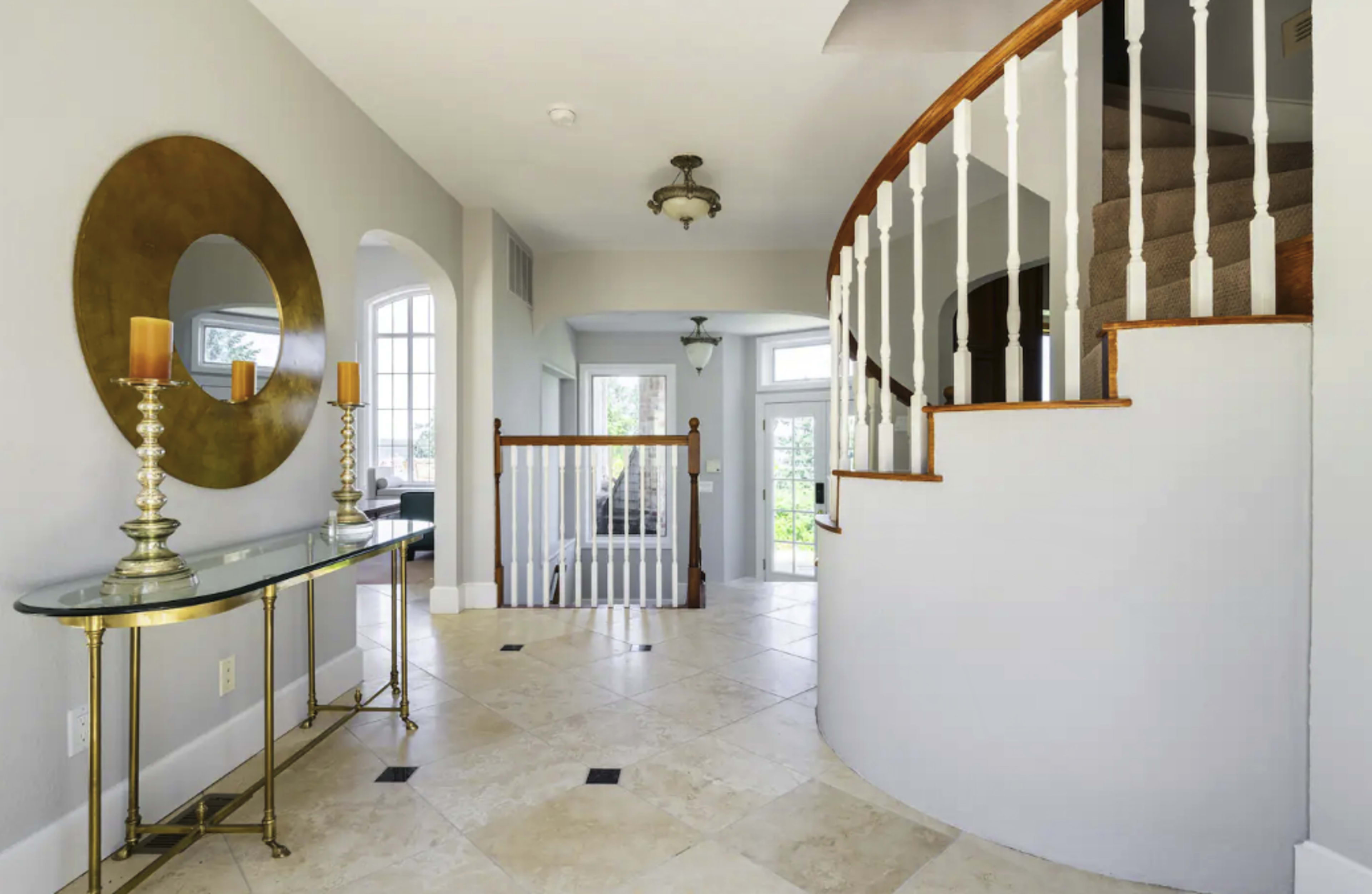 A spacious foyer featuring a curved staircase, a decorative mirror, and a console table with candles.