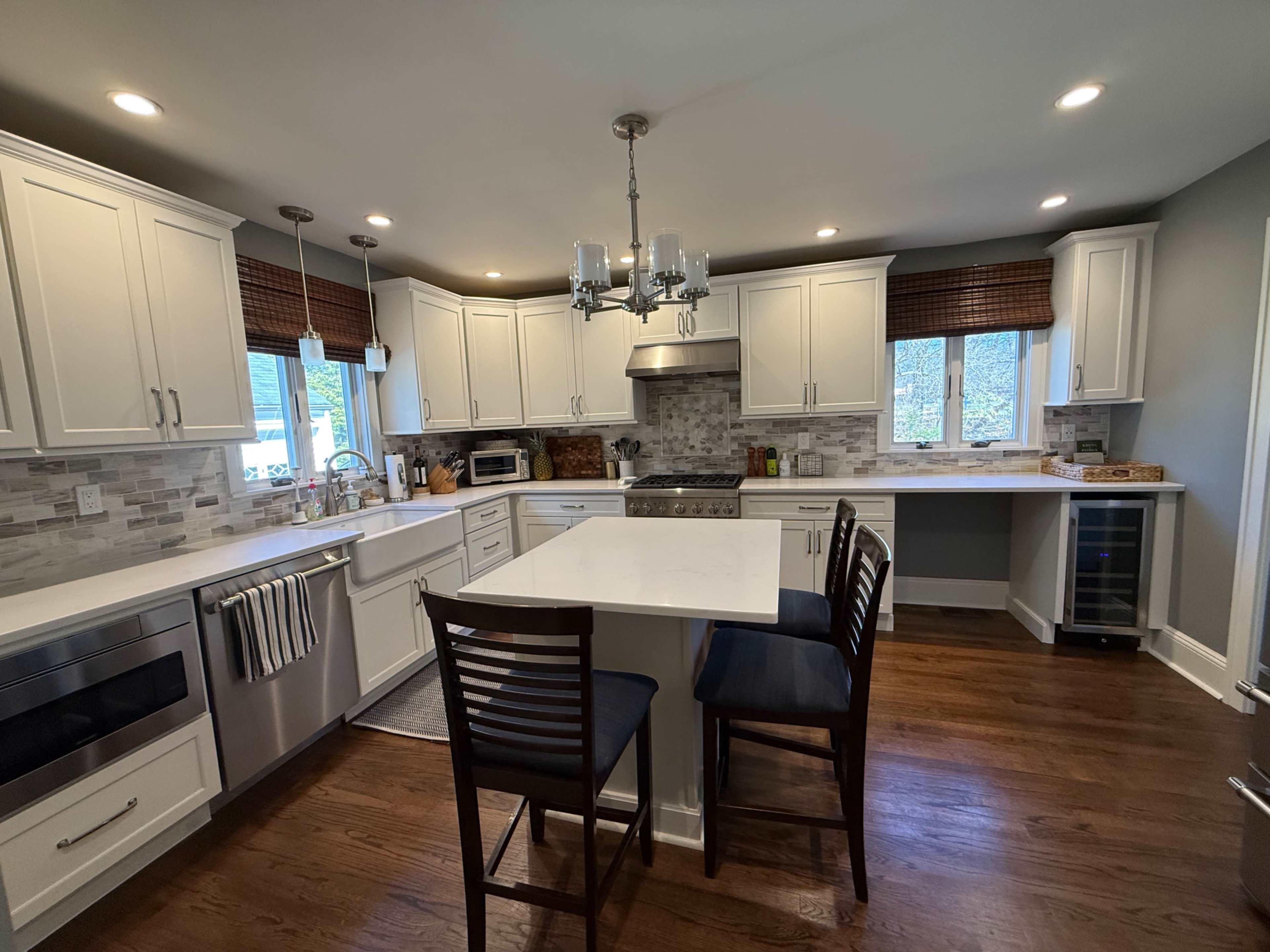 The image shows a modern kitchen featuring white cabinetry, a central island with seating, stainless steel appliances, and hardwood flooring.