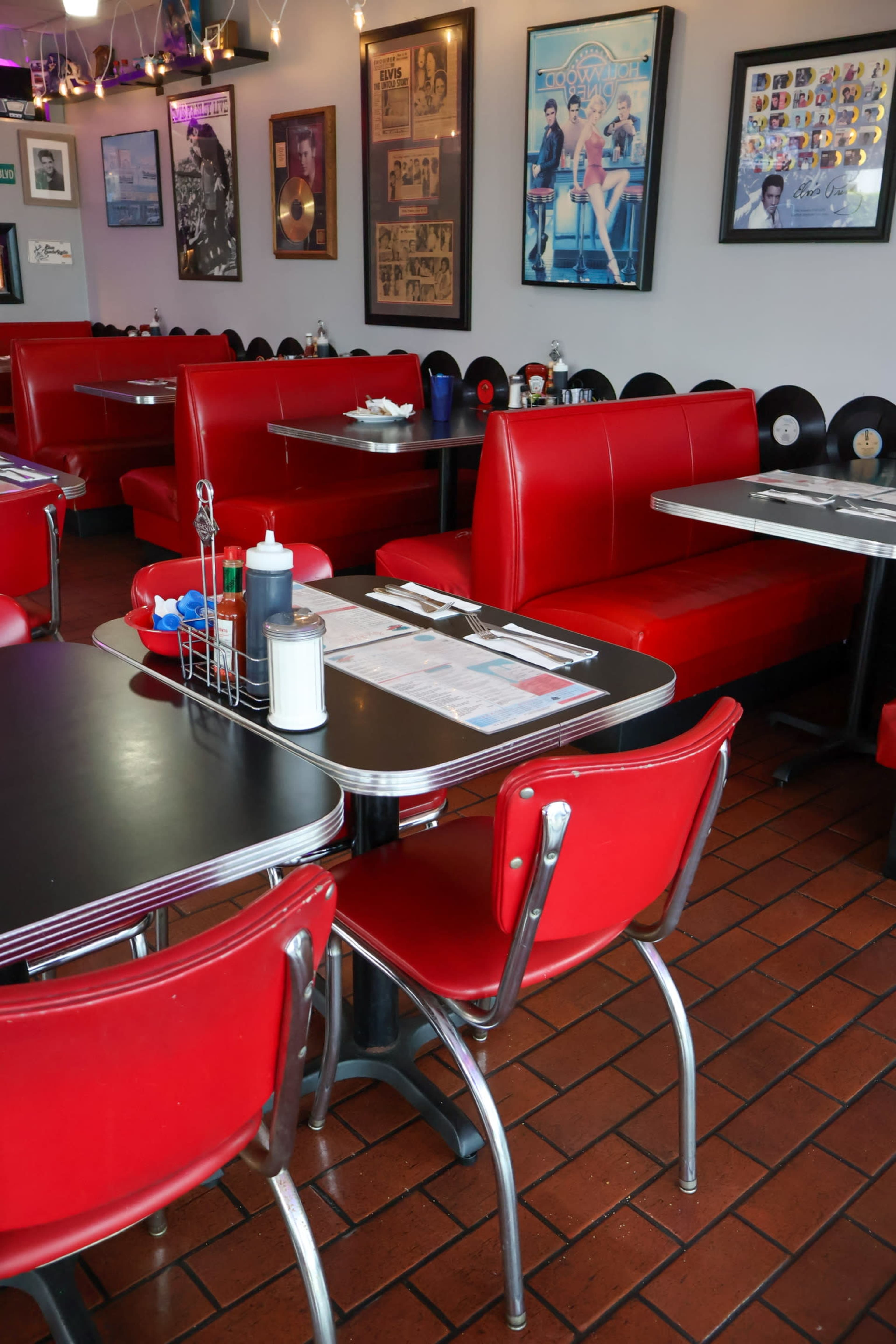 The image shows a retro-style diner with red vinyl booths, black tables, and framed music memorabilia adorning the walls.