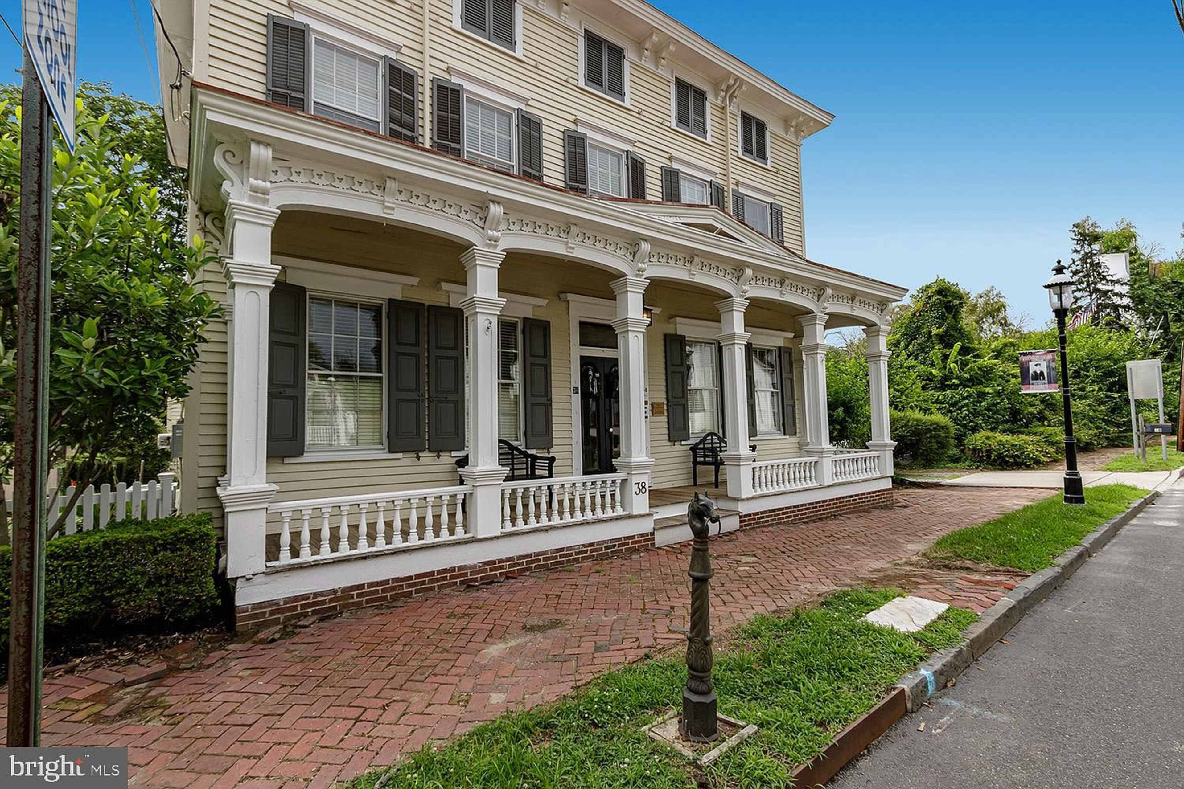 A three-story yellow house with white columns and a brick pathway leading to its entrance.