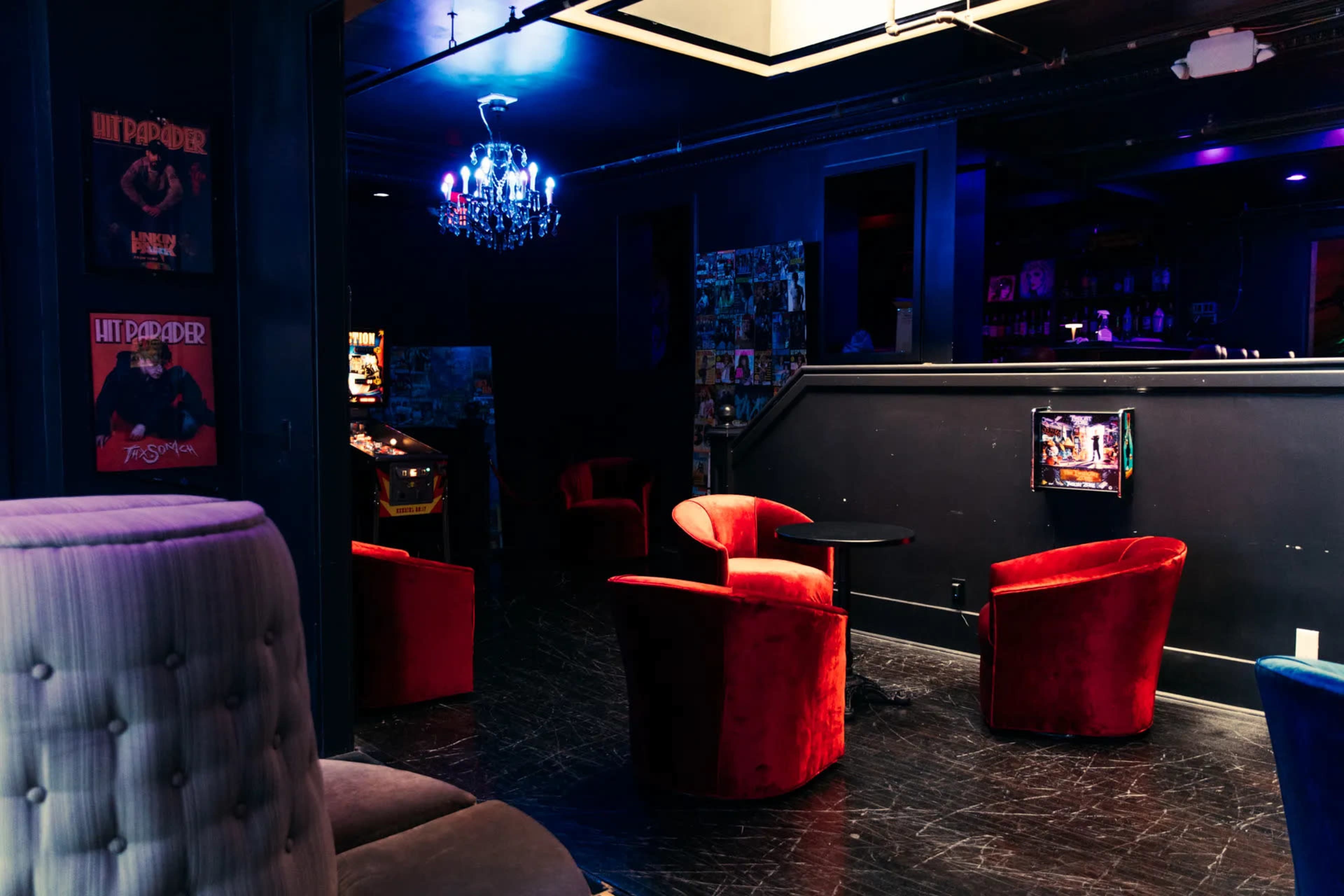 The scene depicts a dimly lit lounge with red velvet chairs, a bar area, and illuminated decor, including a chandelier and arcade games.