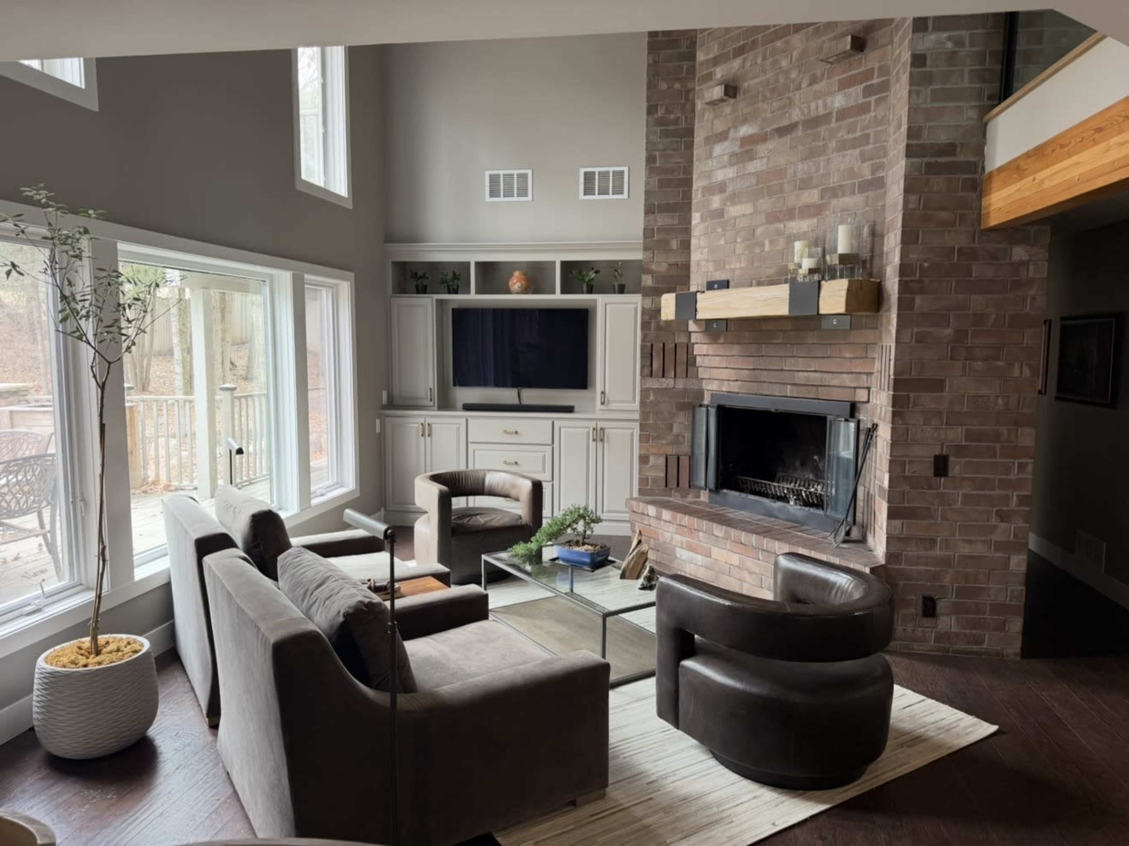 The living room features a brick fireplace, modern furniture, and large windows that provide a view of the outdoors.