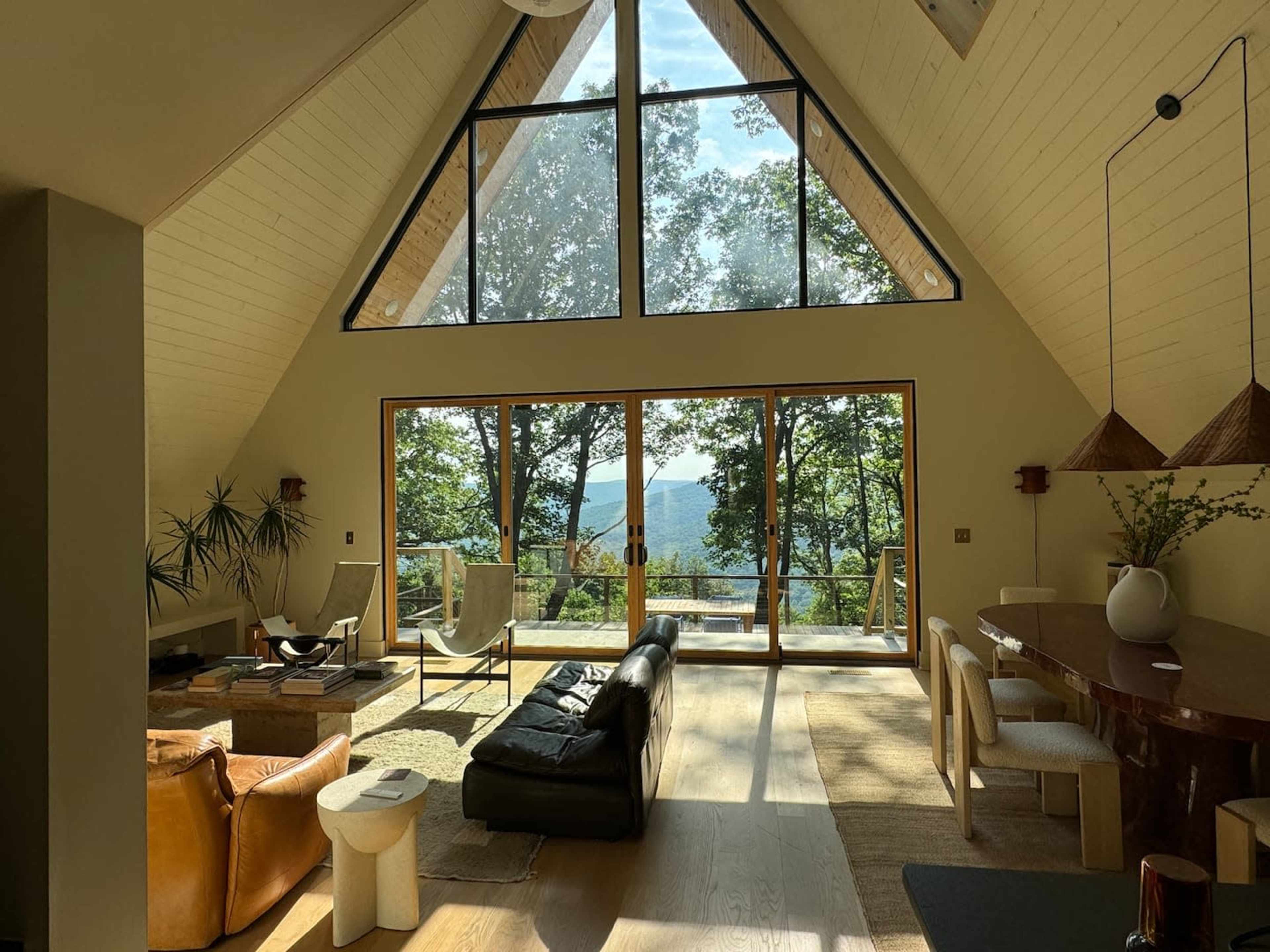 The image shows a spacious, modern living room with large windows overlooking a forested landscape.