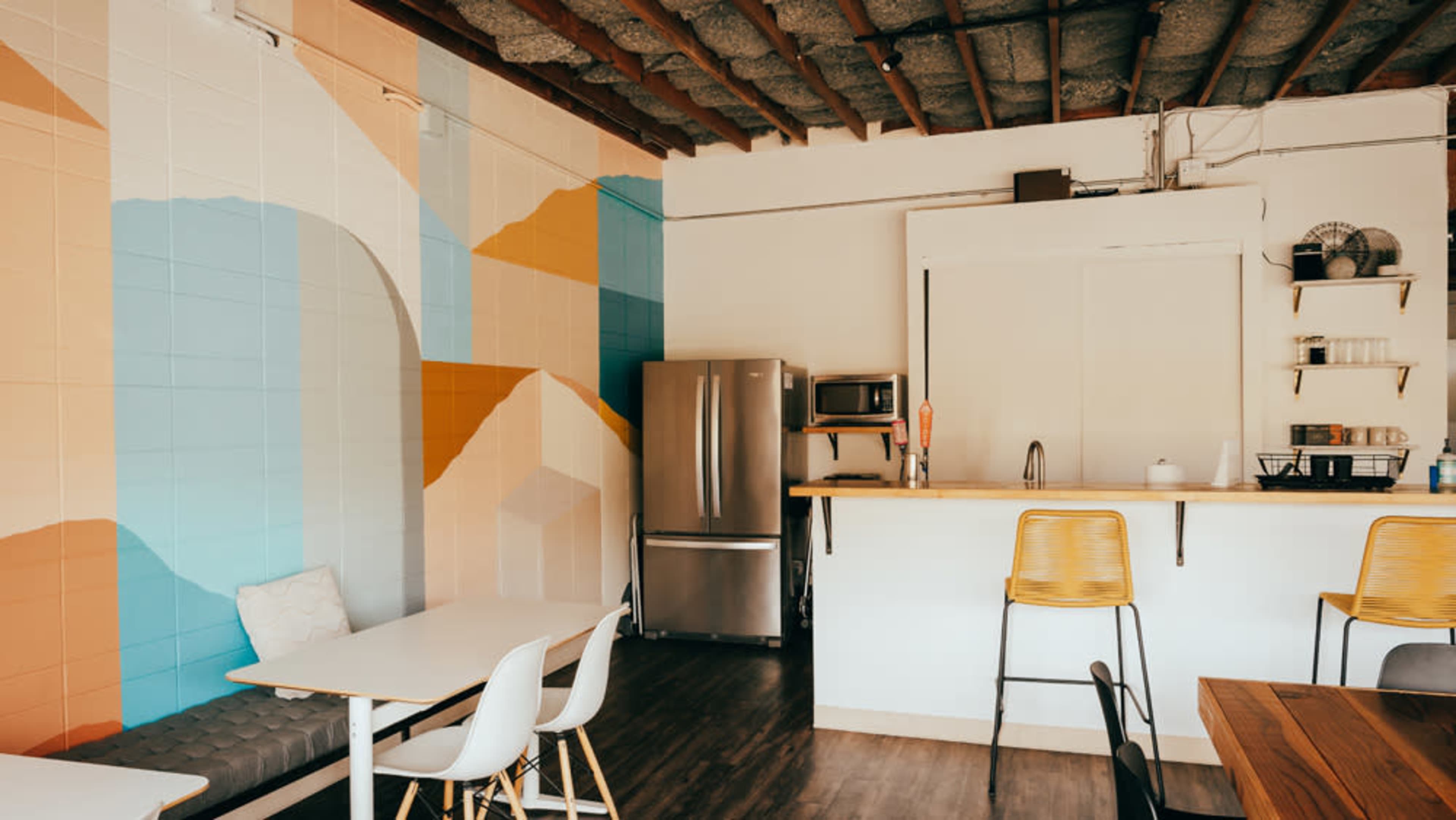 The image shows a modern kitchen area with a colorful mural, stainless steel appliances, and wooden countertops.
