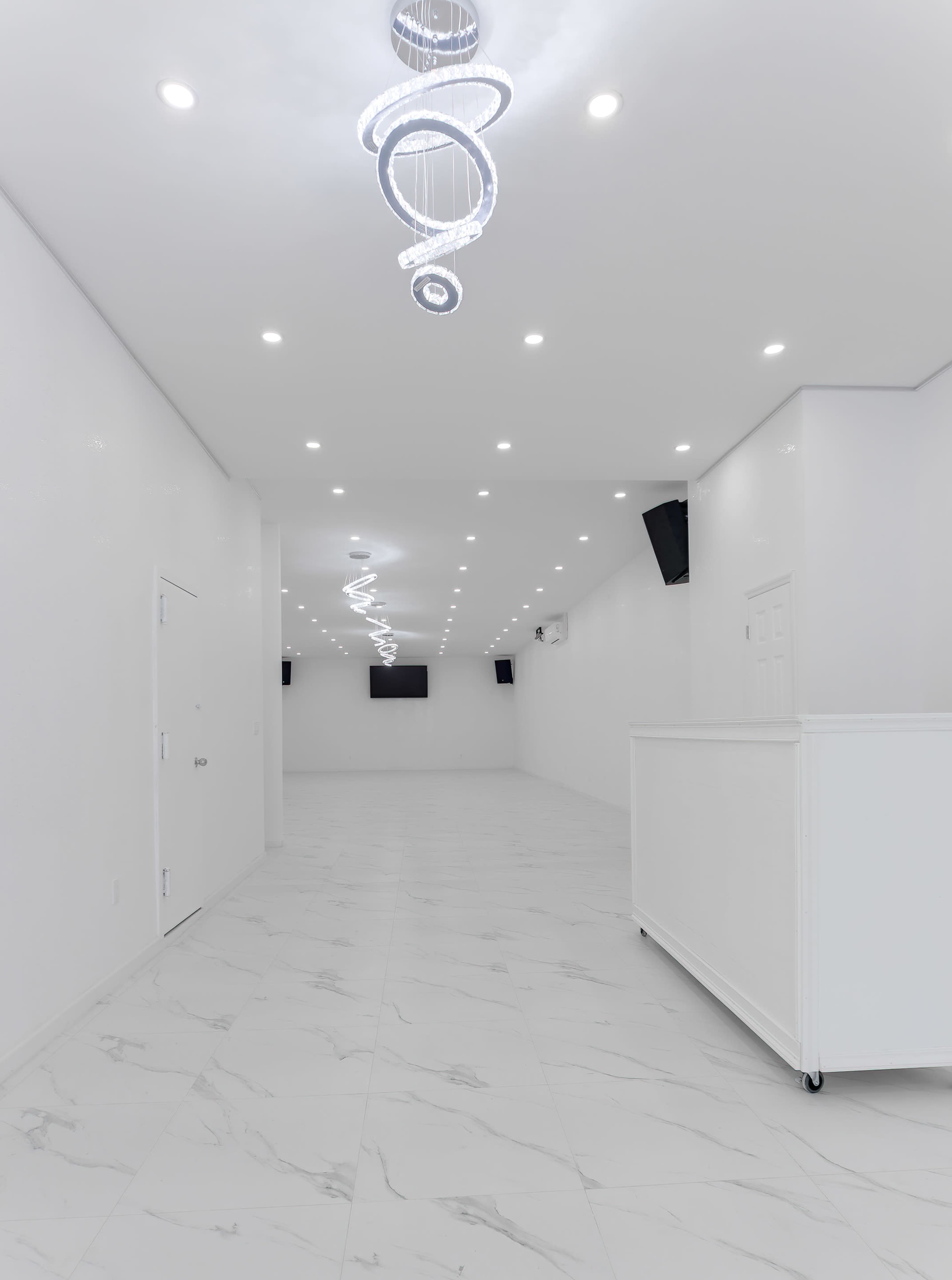 A spacious, well-lit room with white walls, a tile floor, and modern lighting fixtures hanging from the ceiling.