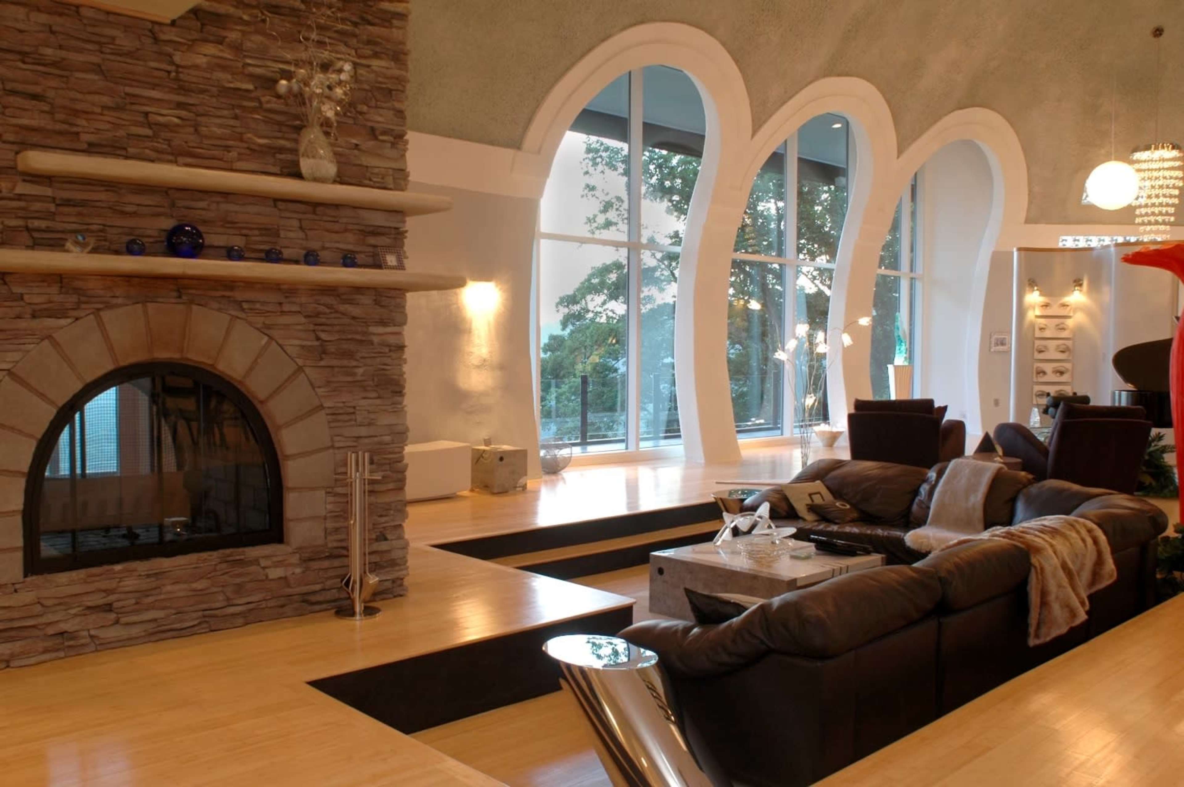 A modern living room with a stone fireplace, large windows, and a sunken seating area featuring a dark sofa and a coffee table.