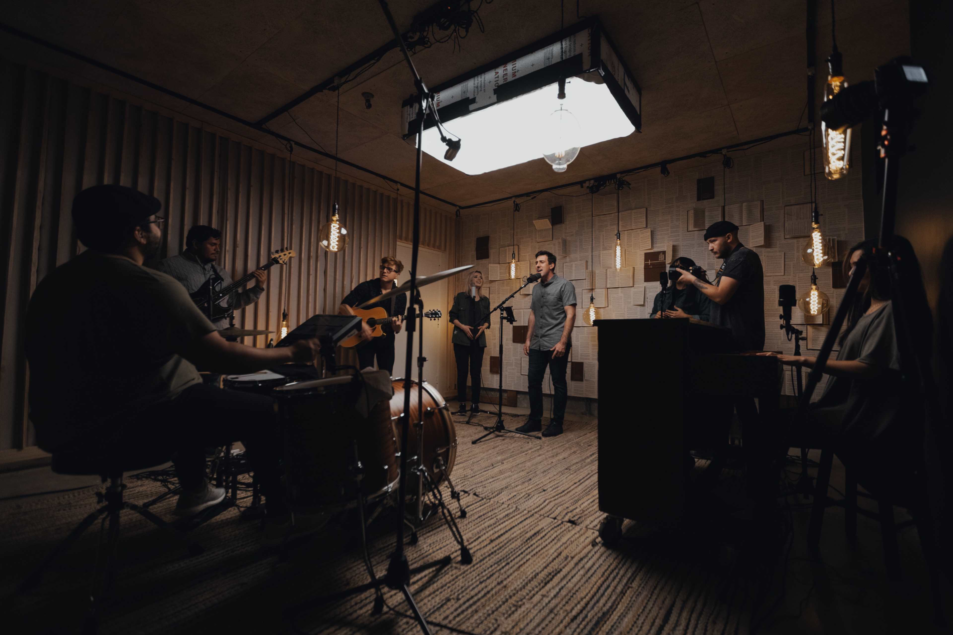 A band performs in a recording studio surrounded by musical instruments and recording equipment.