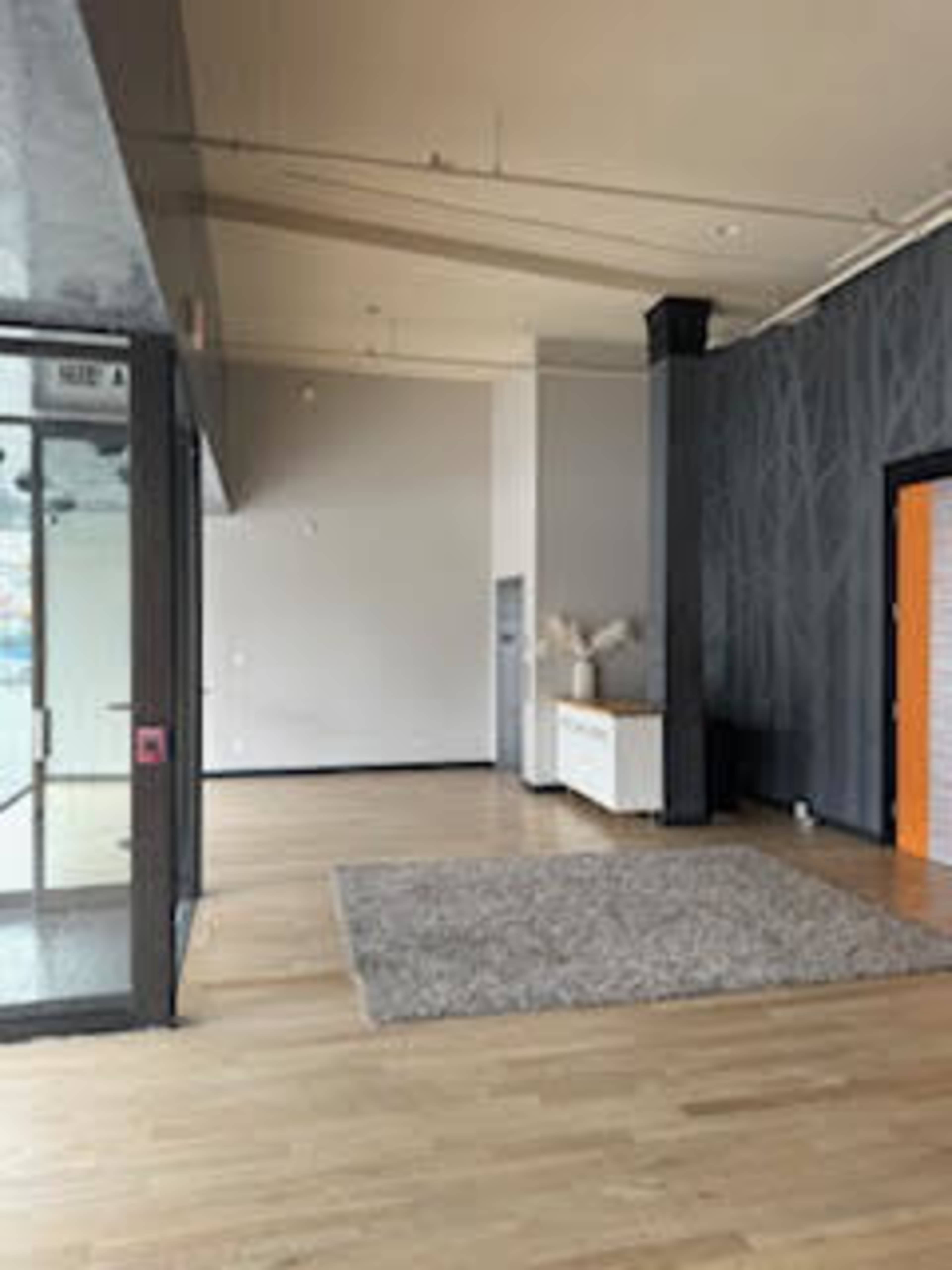 The image shows an empty interior space featuring hardwood floors, a large area rug, a white cabinet, and a wall with a textured pattern.