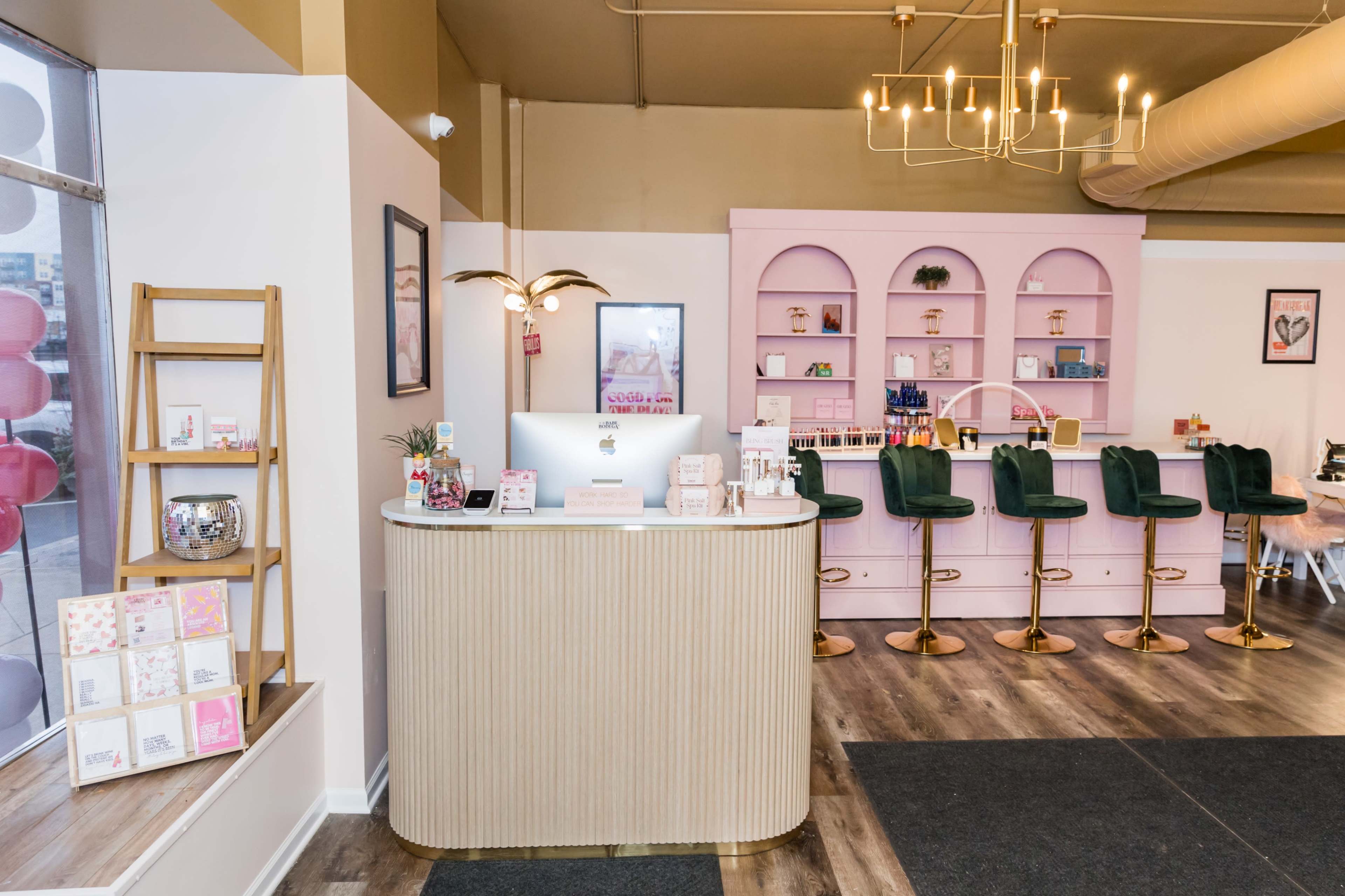 A brightly lit interior featuring a reception desk with a computer and a pink-themed bar area with green stools.