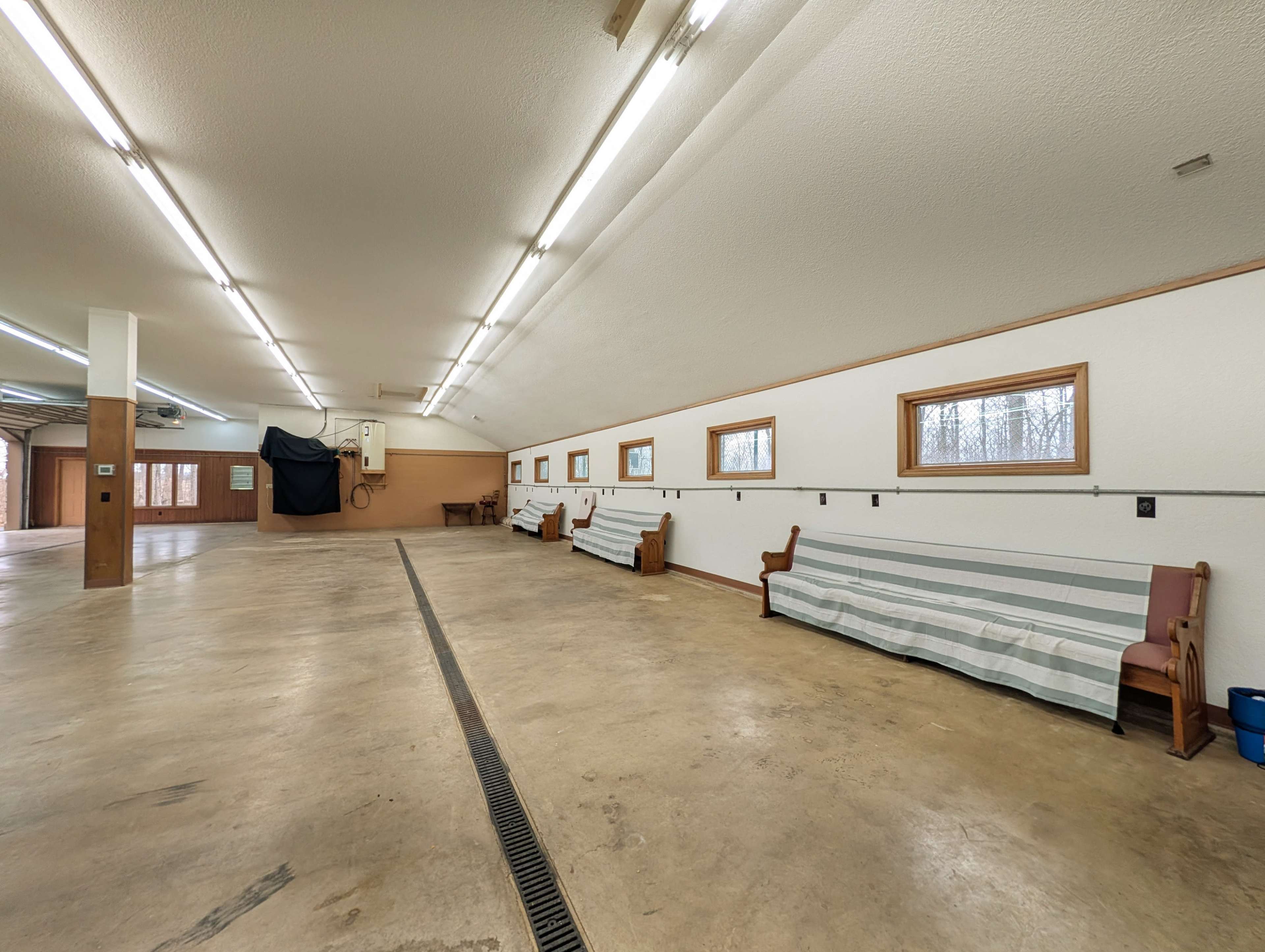 The image shows a spacious, well-lit interior with concrete floors, wooden accents, and several benches along the walls.