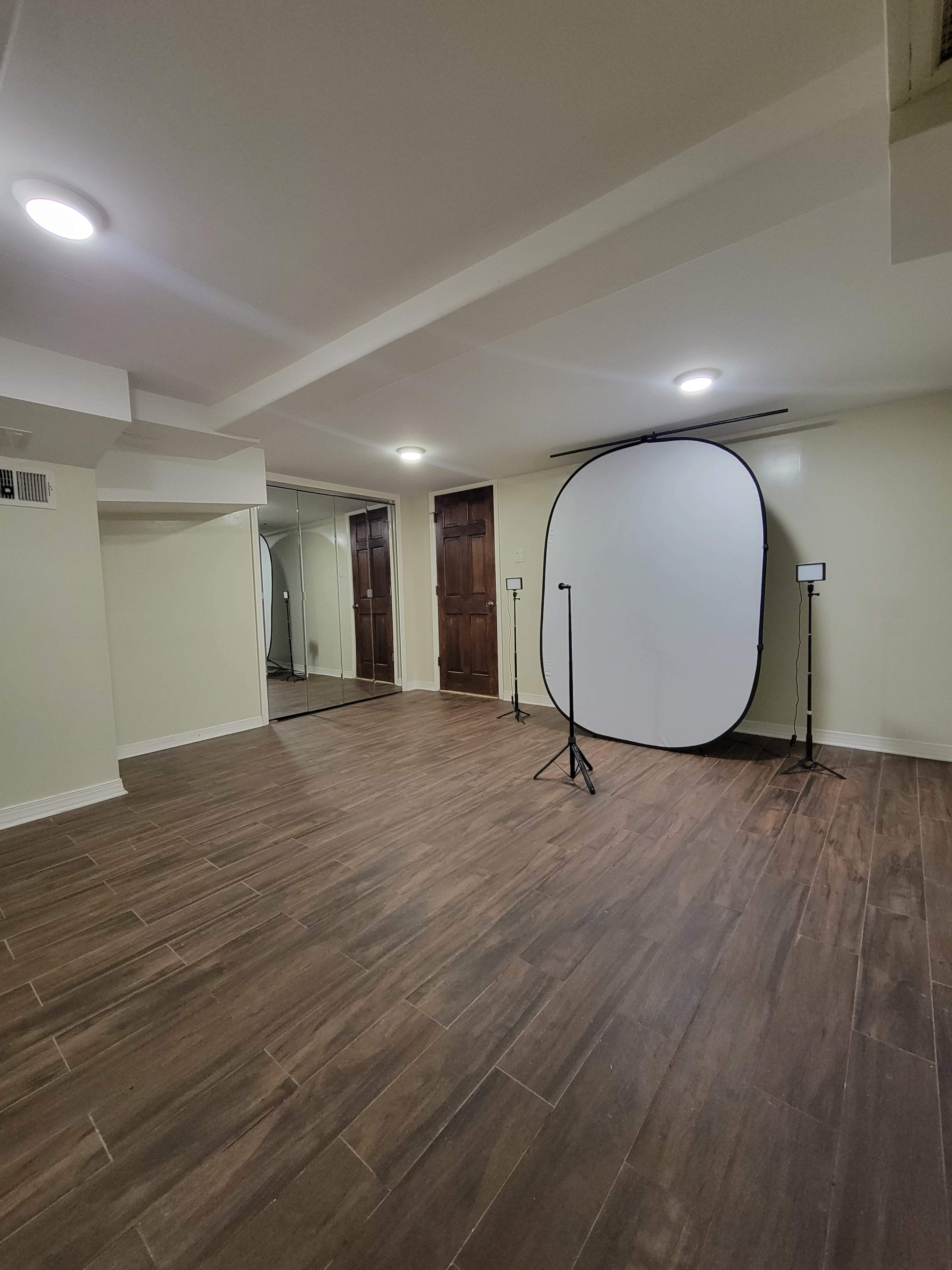 The image shows a spacious room with wooden floors, a large circular backdrop on a stand, and mirrored closet doors along one wall.