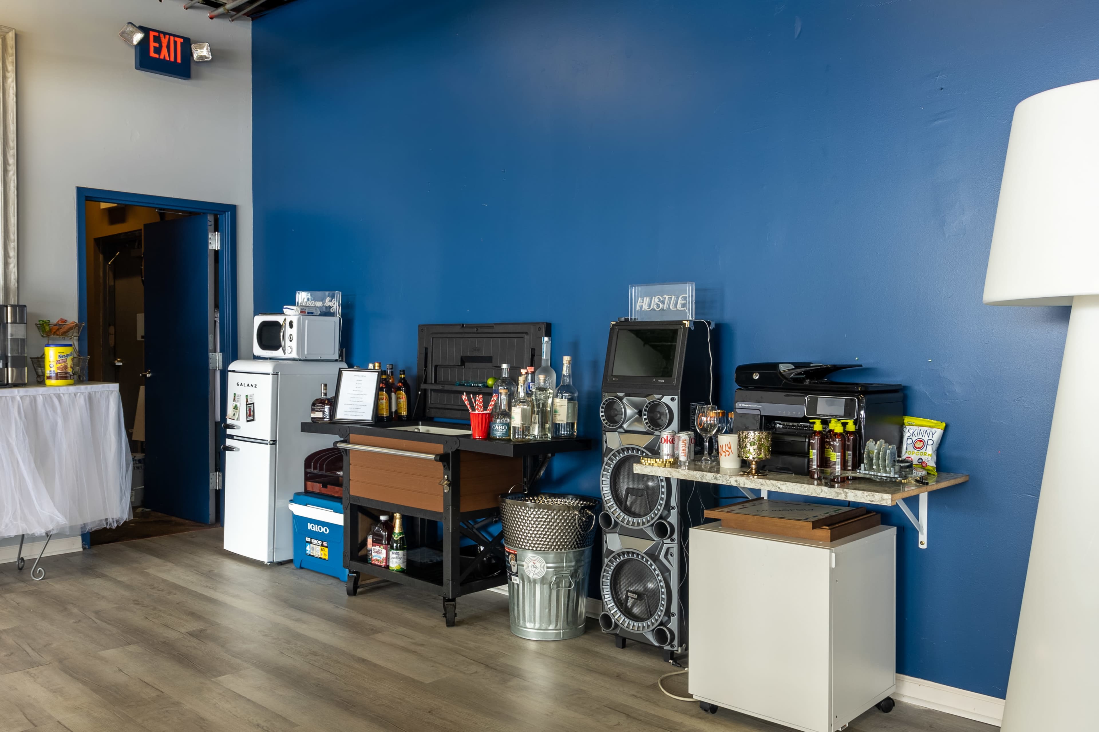 A blue-walled room with a variety of appliances and items on counters, including a microwave, a speaker system, and bins filled with various containers.