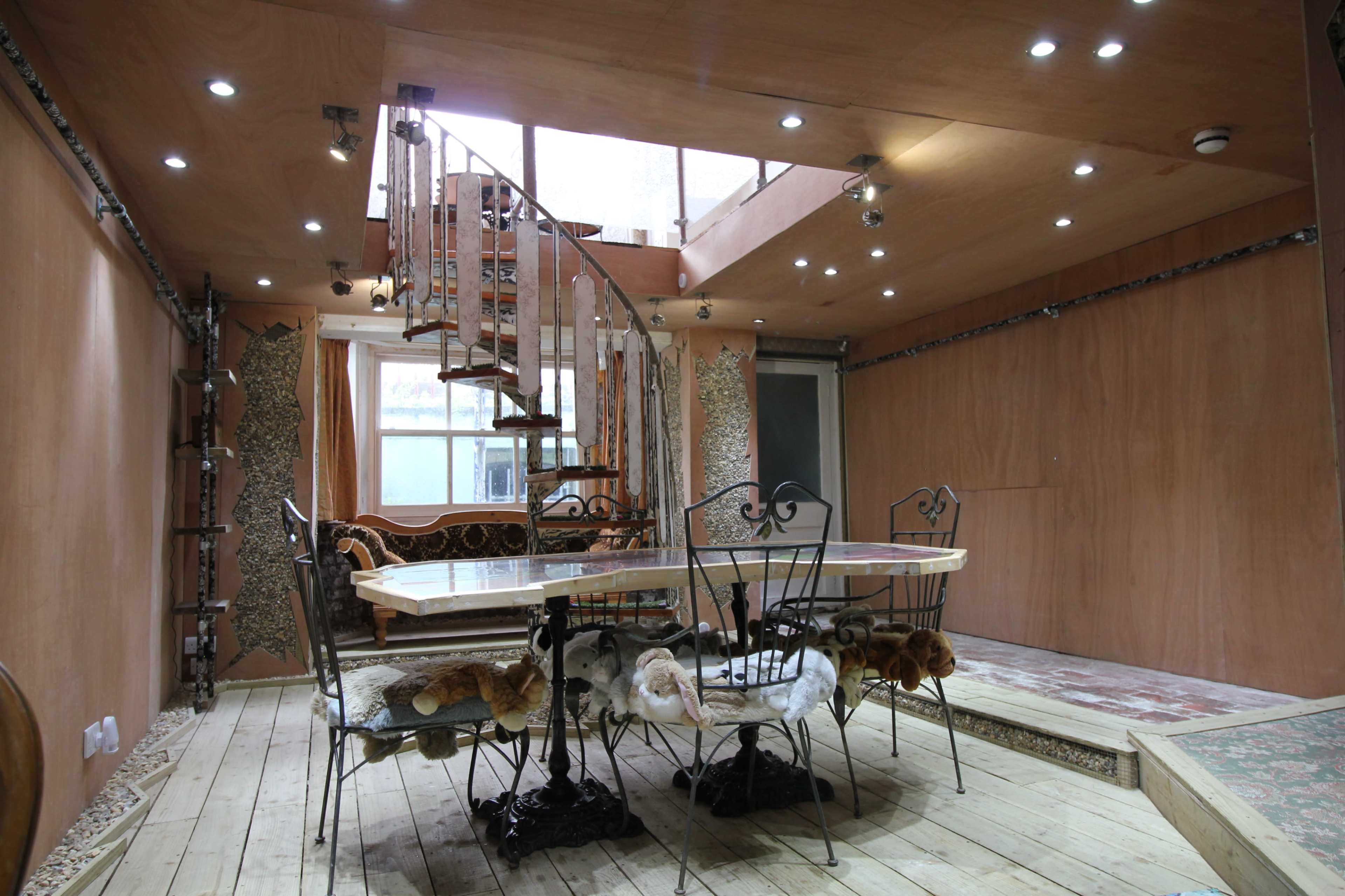 A modern dining area with a spiral staircase, a large wooden table surrounded by ornate chairs, and a wooden floor.