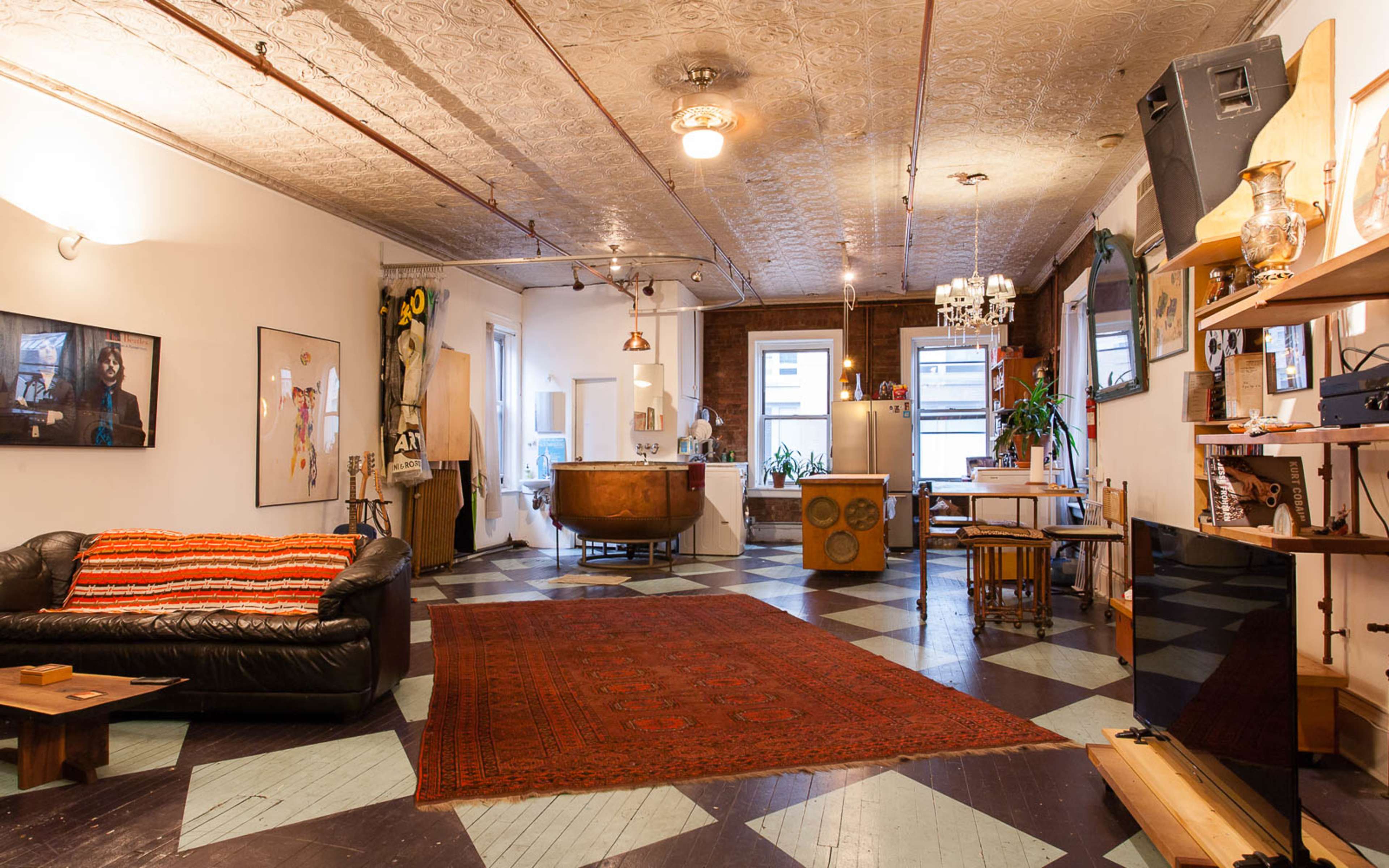 A spacious, eclectic living area featuring a leather sofa, a vintage bathtub, and various decorative items against a patterned floor.