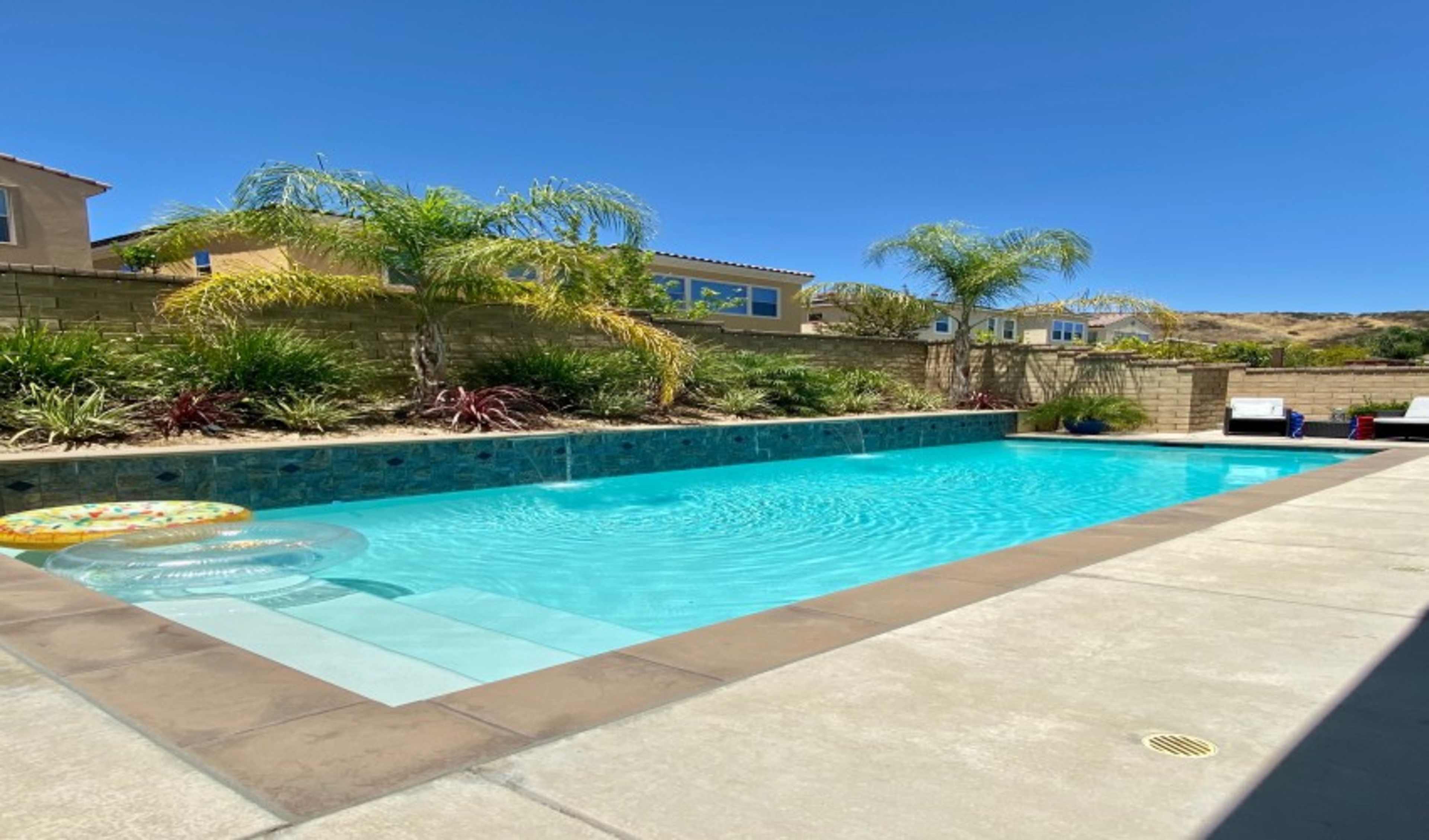 The image shows a swimming pool surrounded by landscaped greenery and houses in the background.
