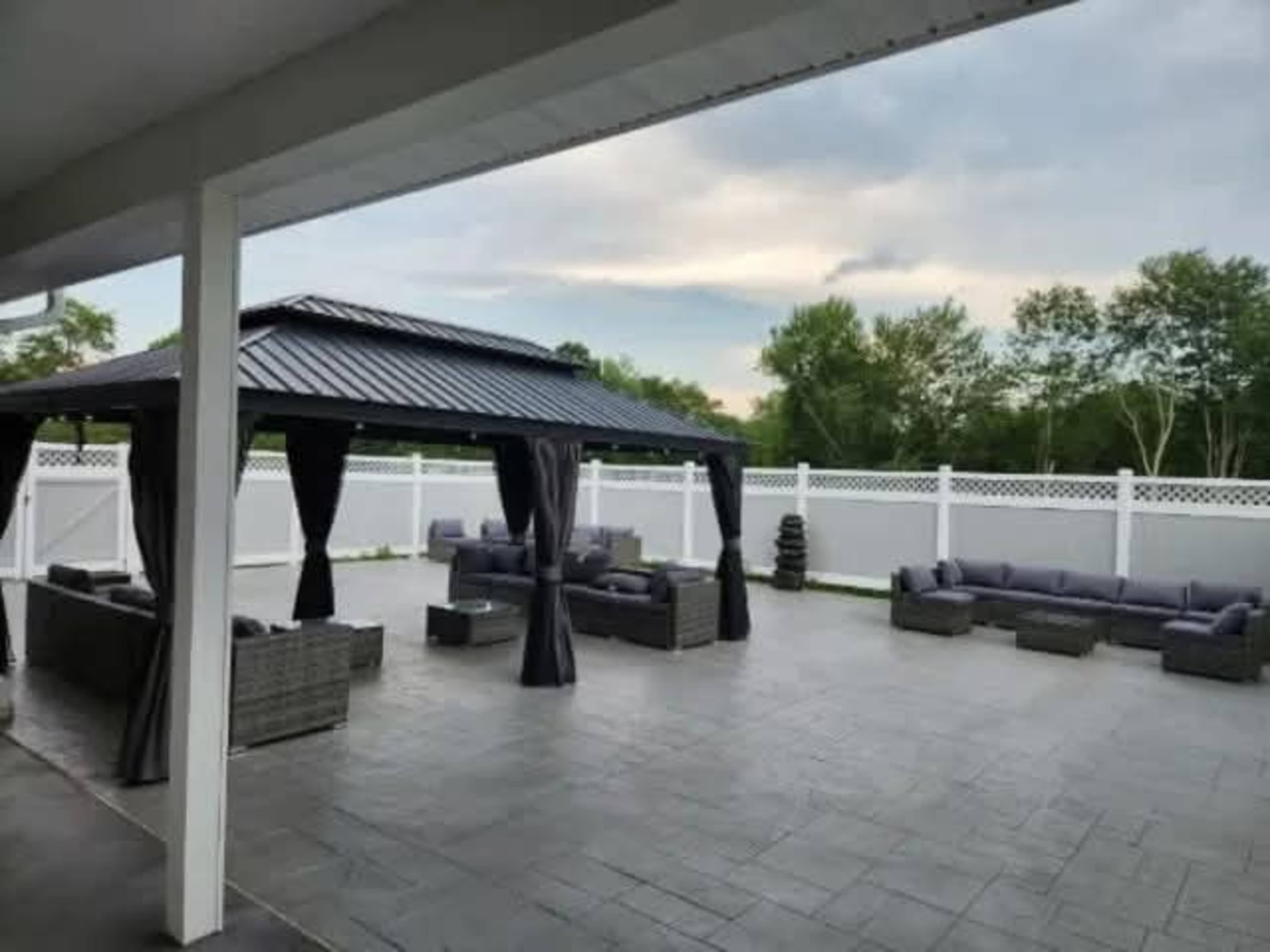 A spacious outdoor patio features a gazebo with draped curtains, surrounded by comfortable seating and a white vinyl fence.