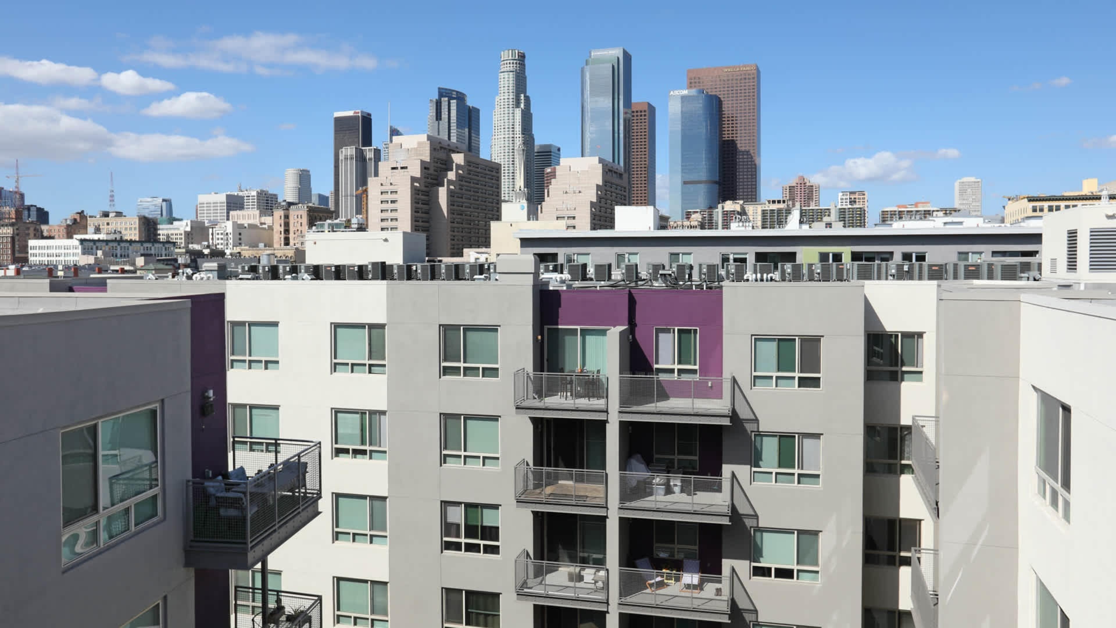 A view of modern apartment buildings with balconies in the foreground and a skyline of high-rise buildings in downtown Los Angeles in the background.