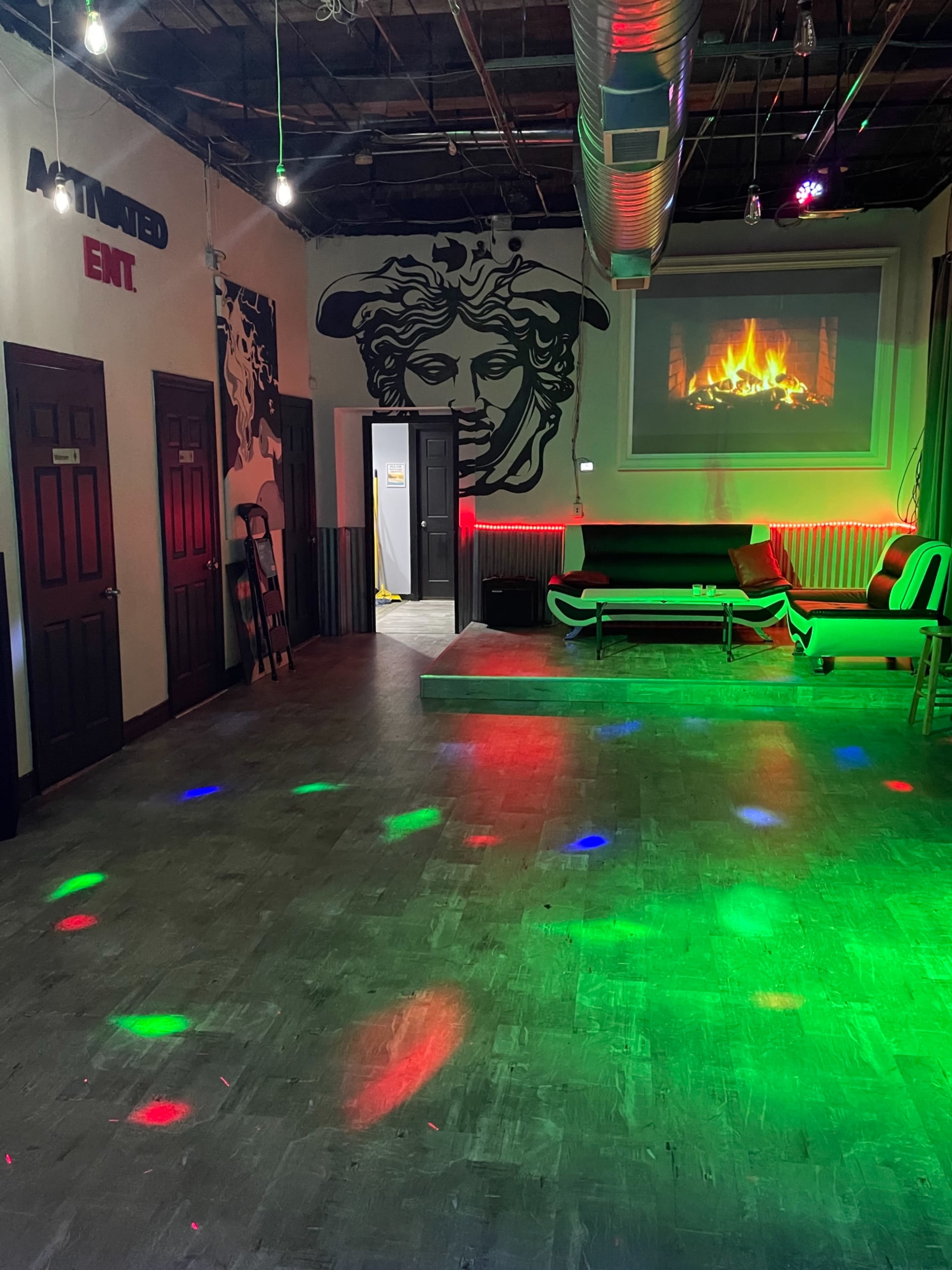 A dimly lit lounge area featuring a fireplace projection on the wall, decorative lighting, and a minimalist seating arrangement.