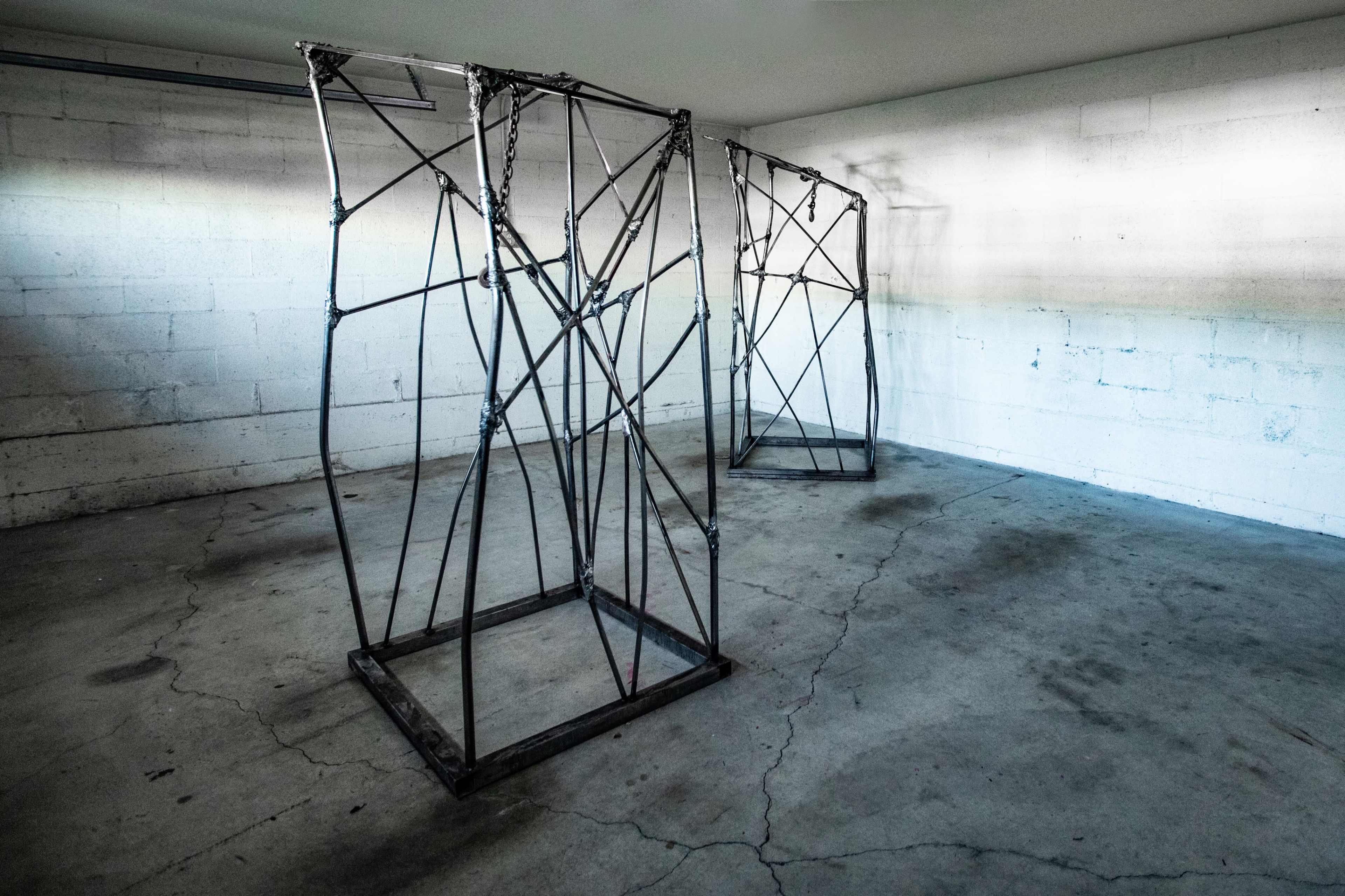 Two large metal frame structures positioned in an empty indoor space with a concrete floor and bare walls.
