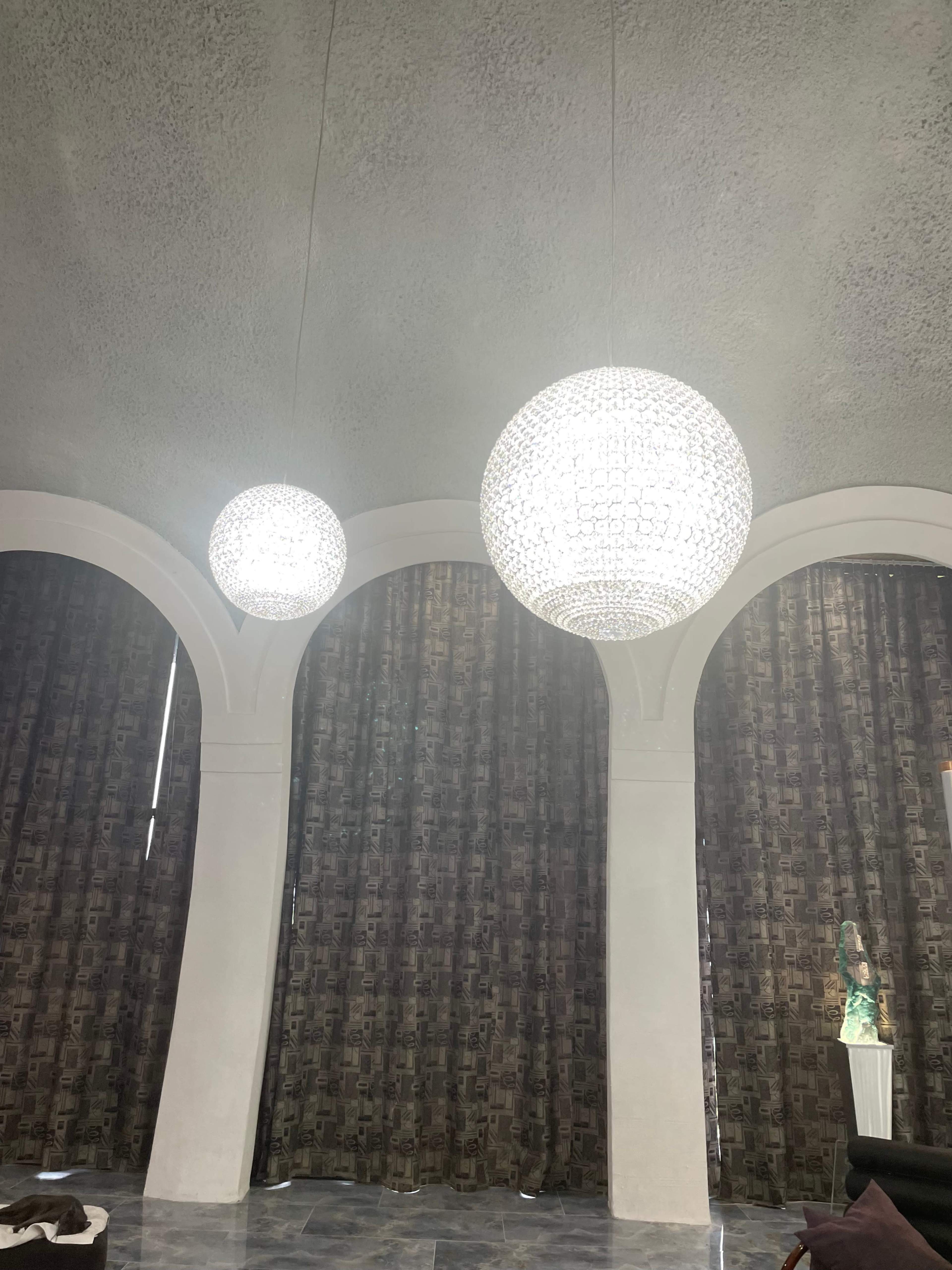 A room with two large chandelier lights hanging from a textured ceiling, flanked by dark drapes and a decorative statue on a pedestal.