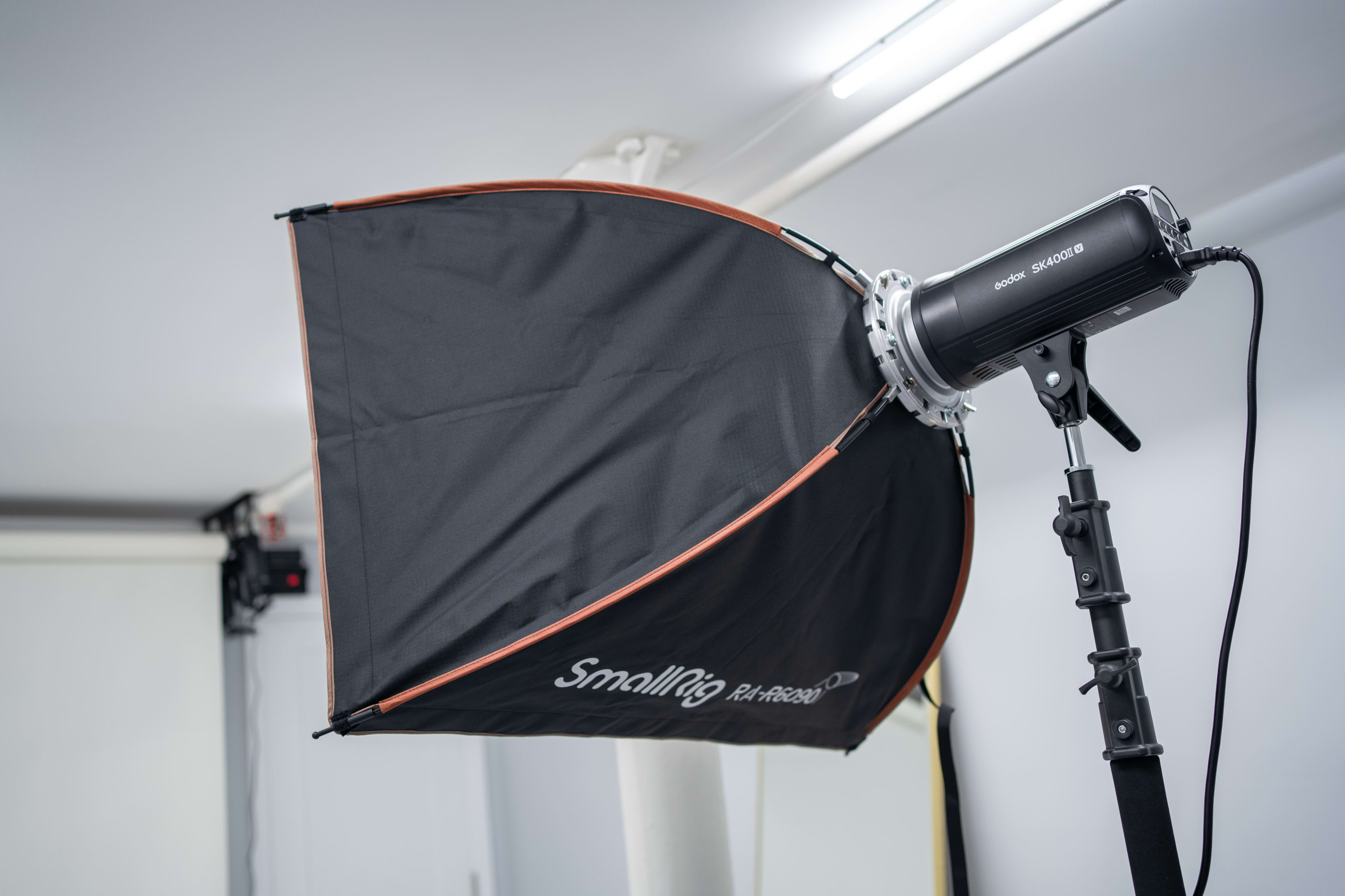 A black softbox with an umbrella shape is attached to a photography light stand in a studio setting.