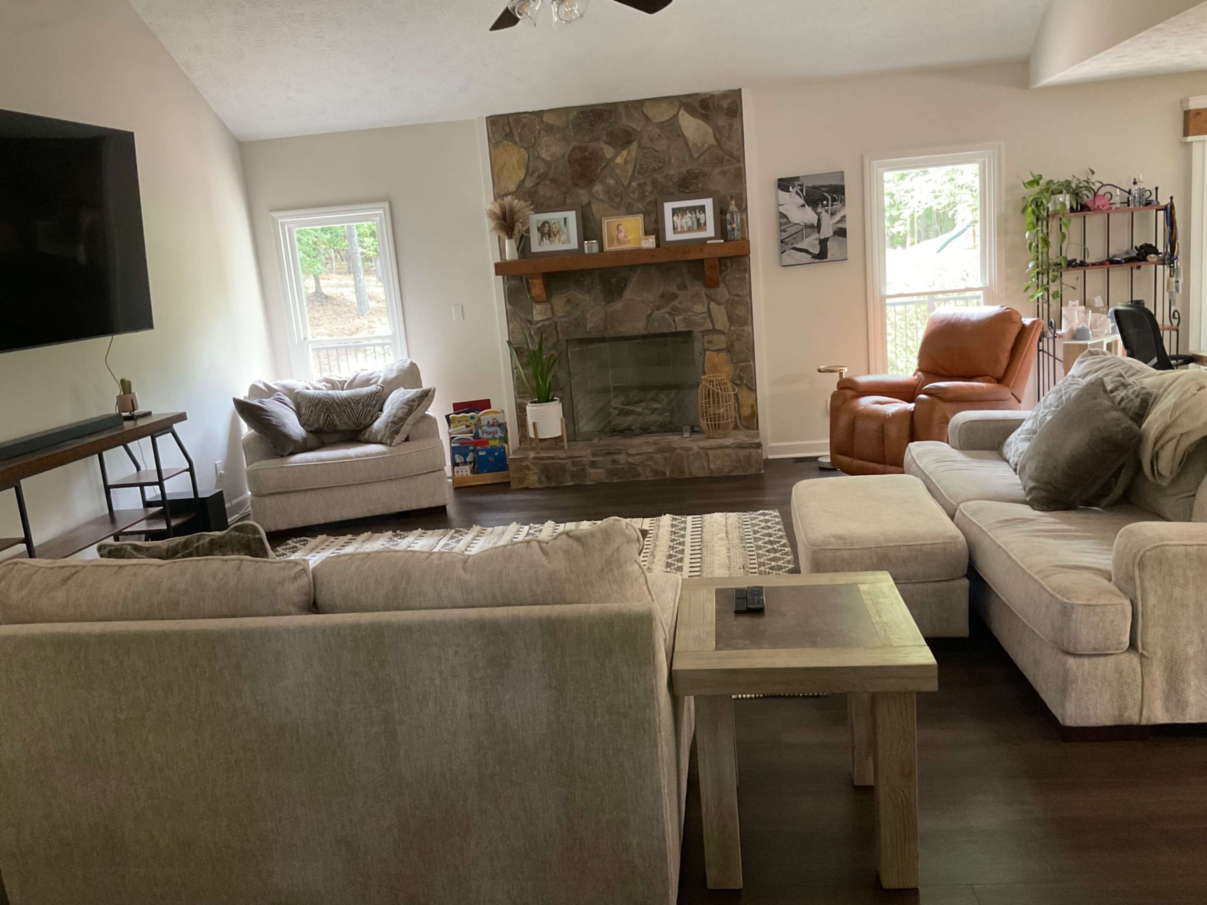 The living room features a stone fireplace, two chairs, a large sectional sofa, and a television mounted on the wall.