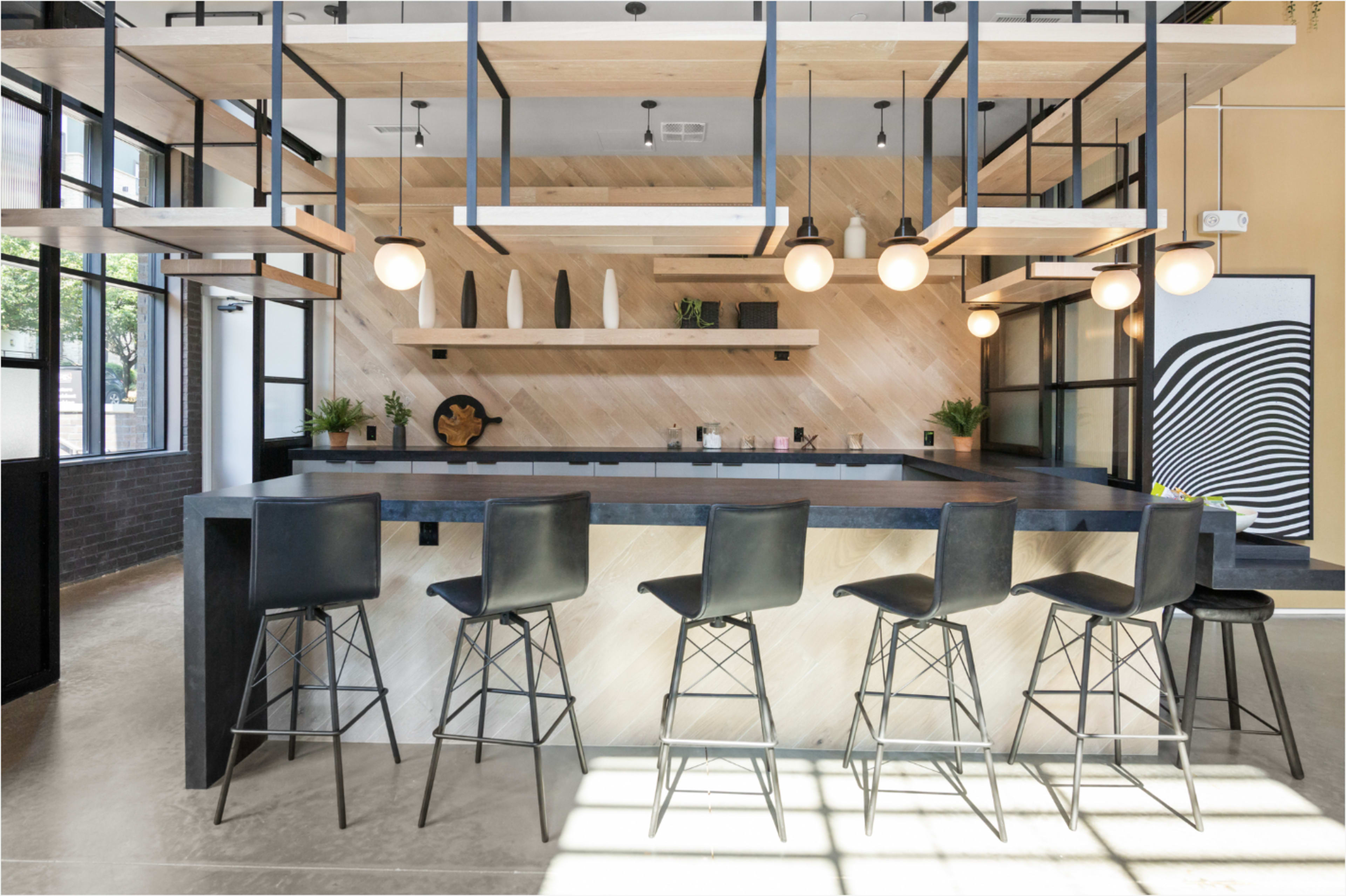 The image features a modern bar area with a sleek counter and six black stools, surrounded by wood accents and pendant lighting.