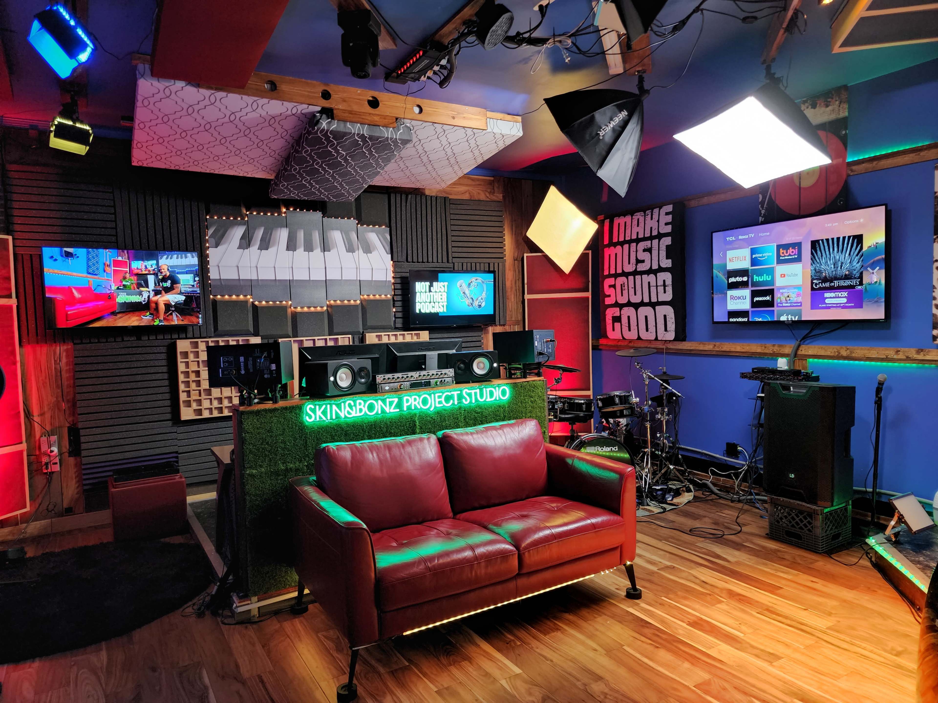 The image shows a vibrant music studio with a red leather couch, audio equipment, and multiple screens displaying music-related content.