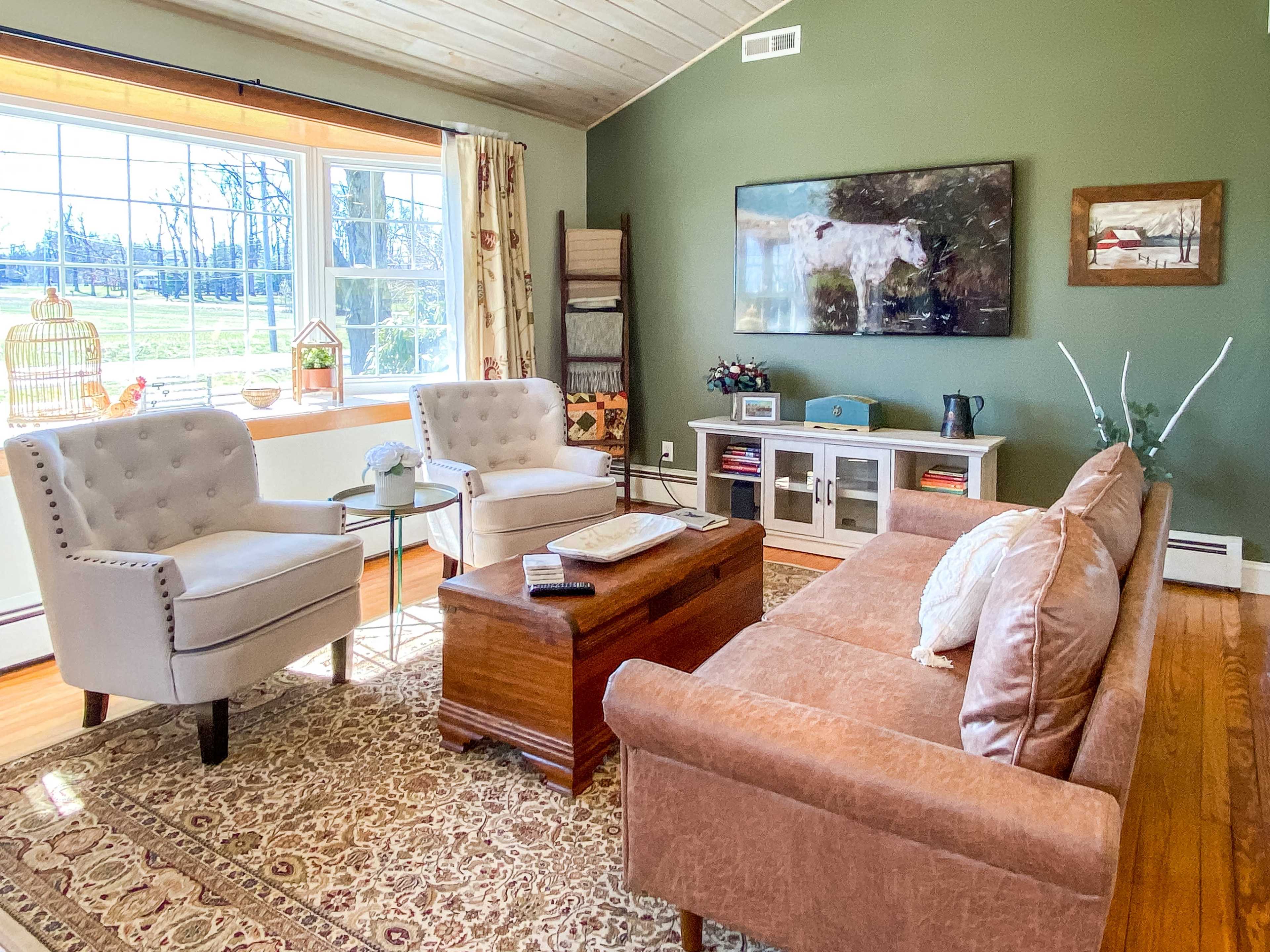 A living room with two armchairs, a coffee table, and a couch arranged around a large window that overlooks a green space.