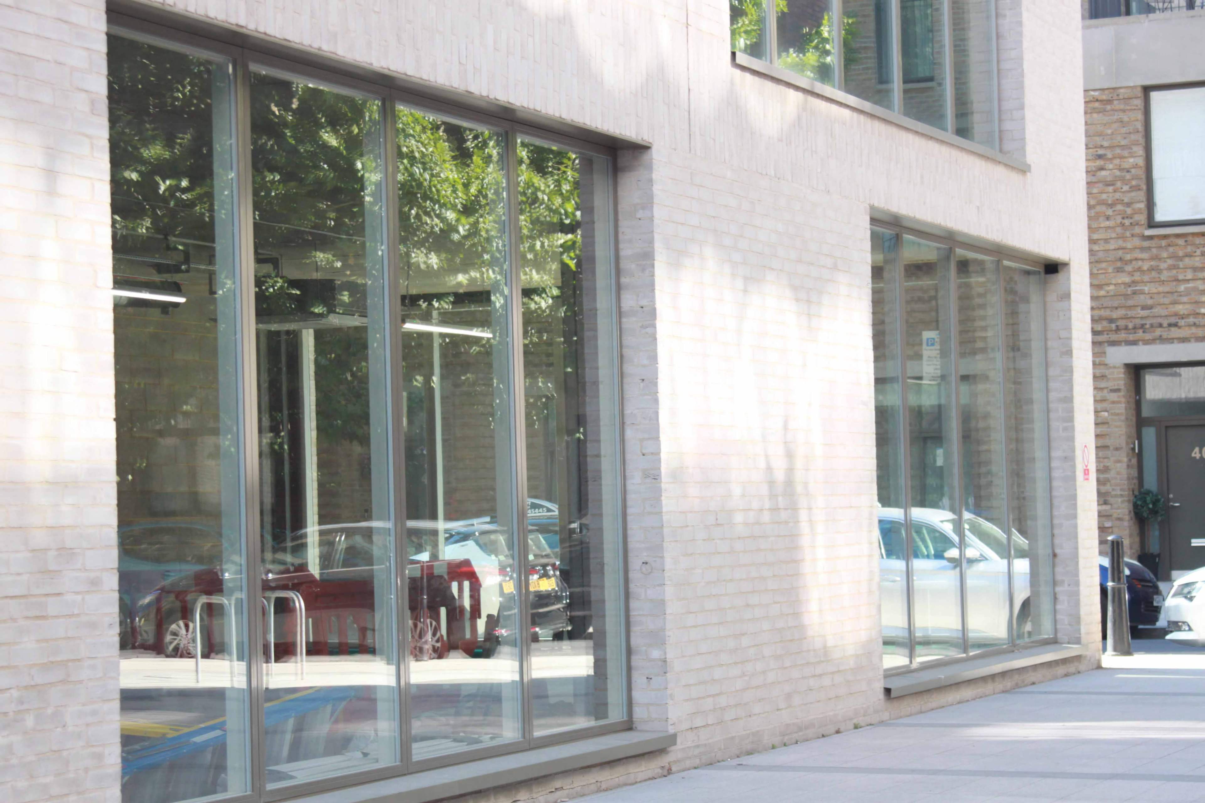 A wall with large glass windows reflecting cars and trees in a modern urban setting.